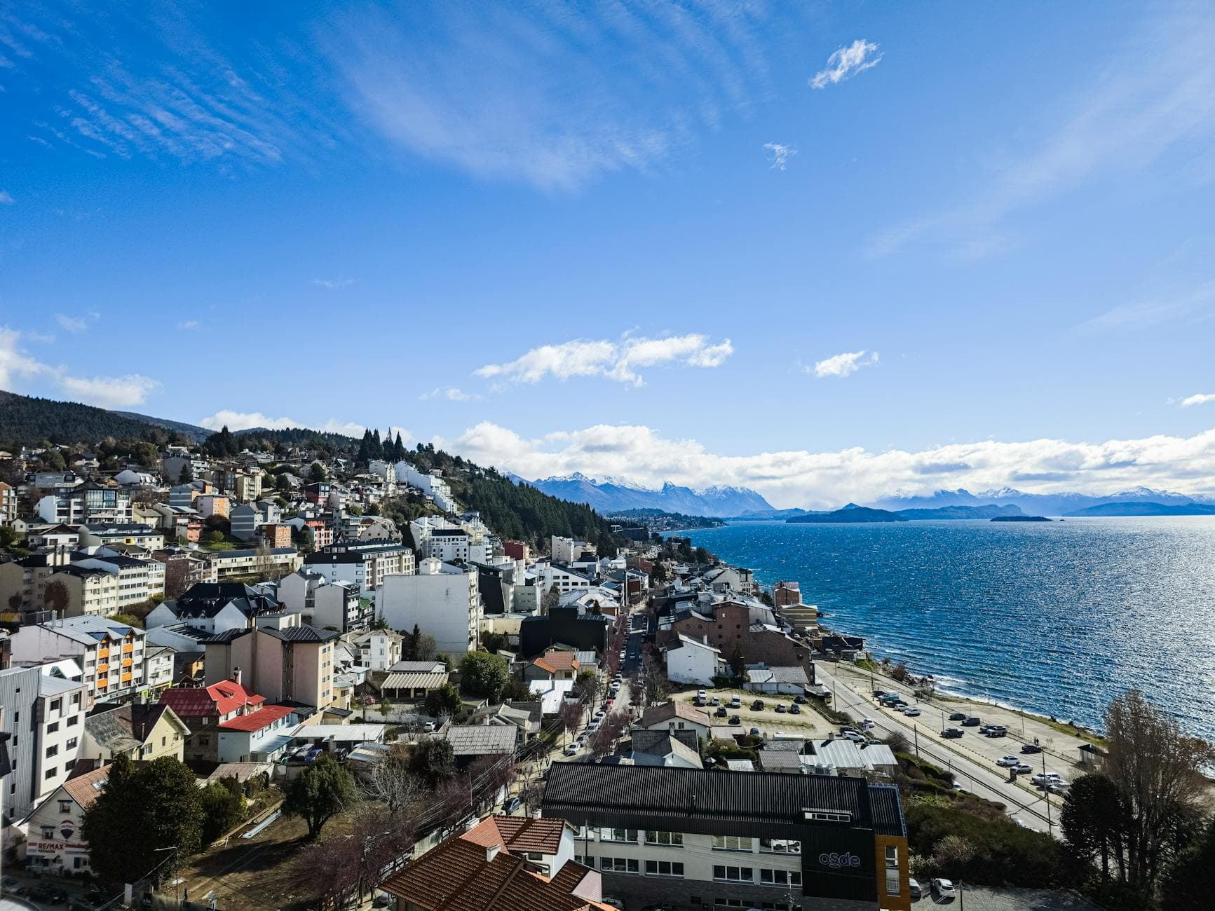 Scenic aerial view of San Carlos de Bariloche with cityscape and lake under a bright blue sky.