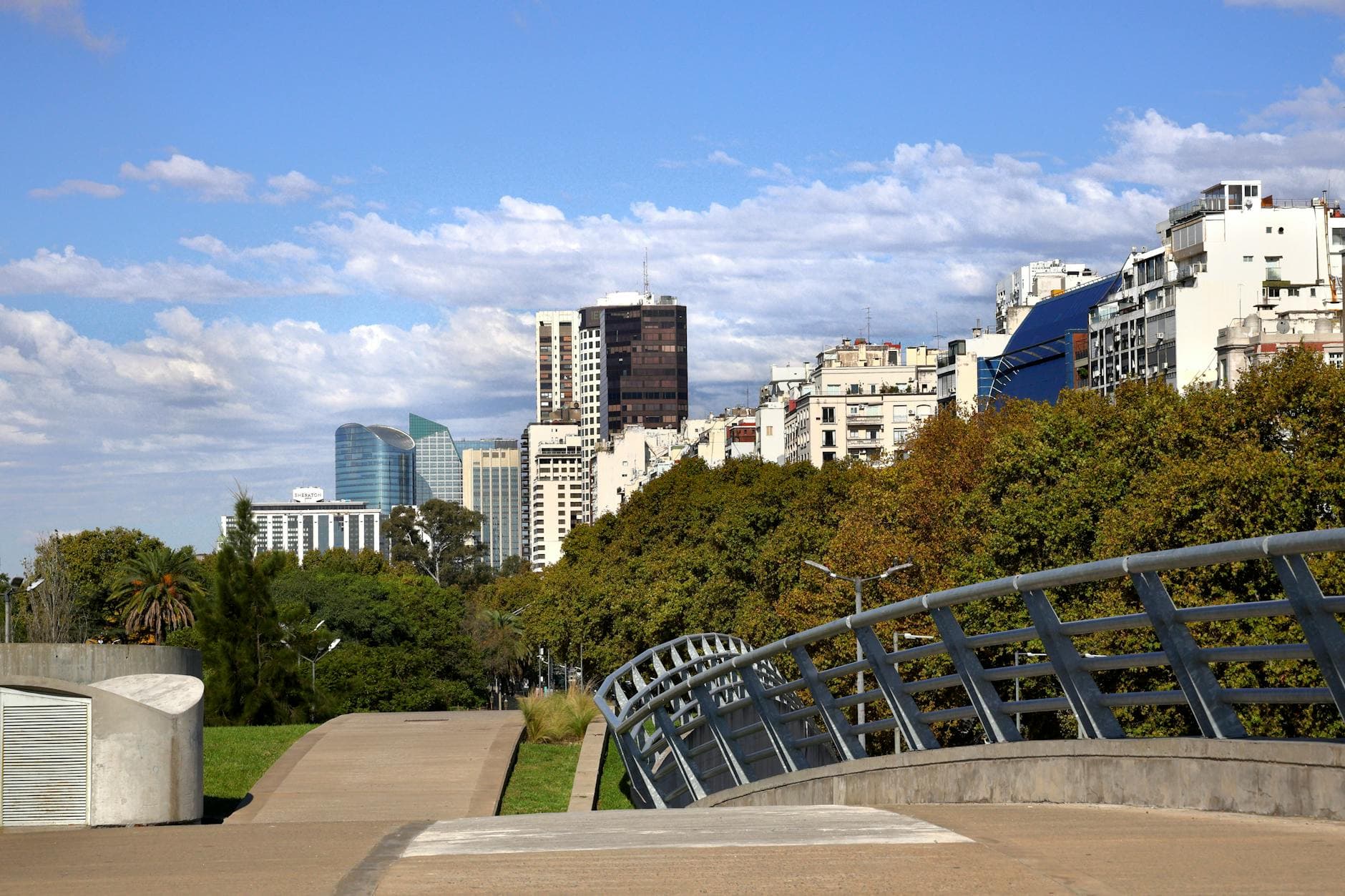 Skyline view of Buenos Aires with modern buildings, lush greenery, and a pedestrian bridge on a clear day.