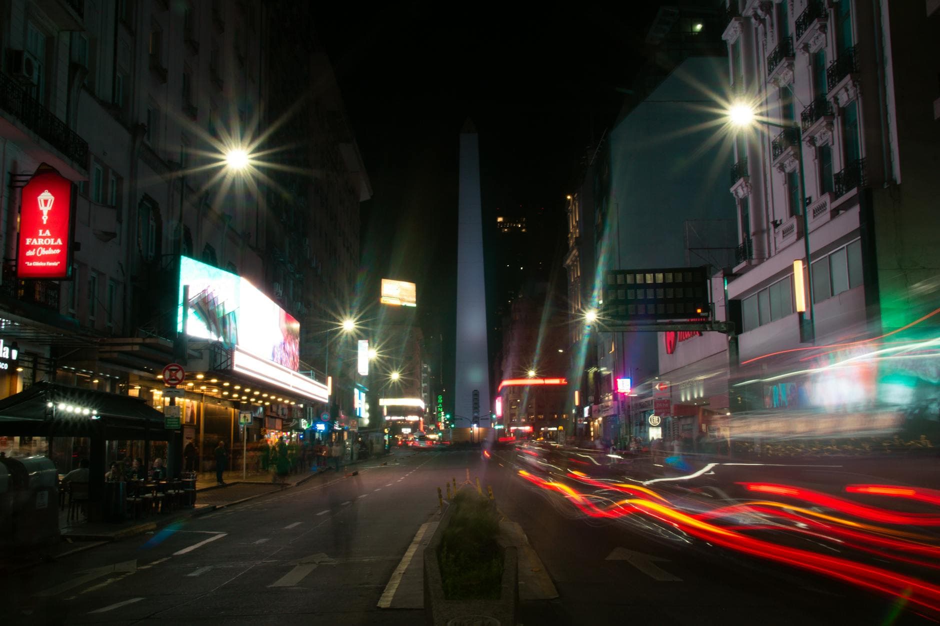 Long-exposure night shot of the Obelisk in Buenos Aires with colorful light trails on a bustling street.