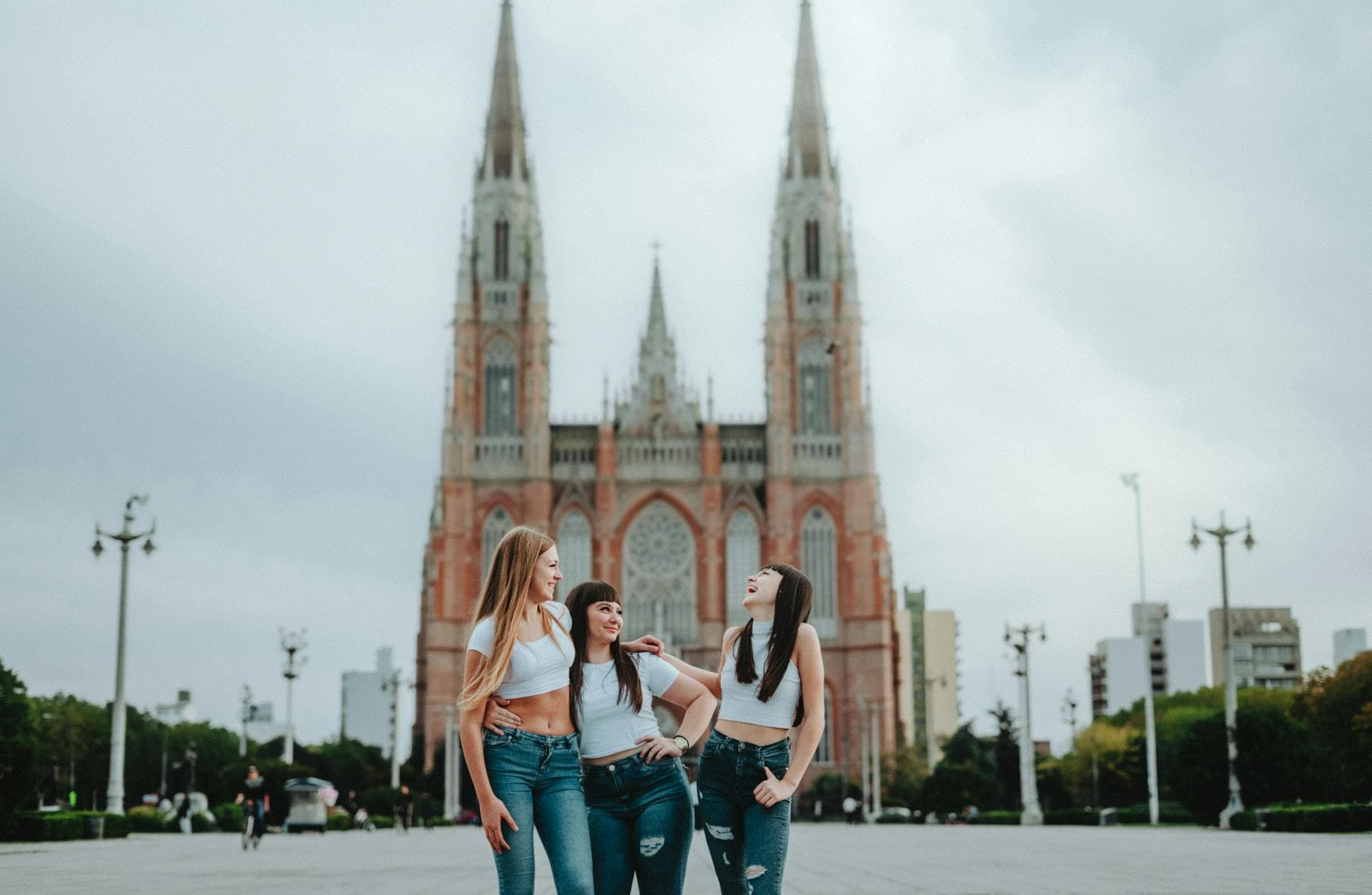 Three women share a joyful moment in front of the iconic La Plata Cathedral, Argentina.