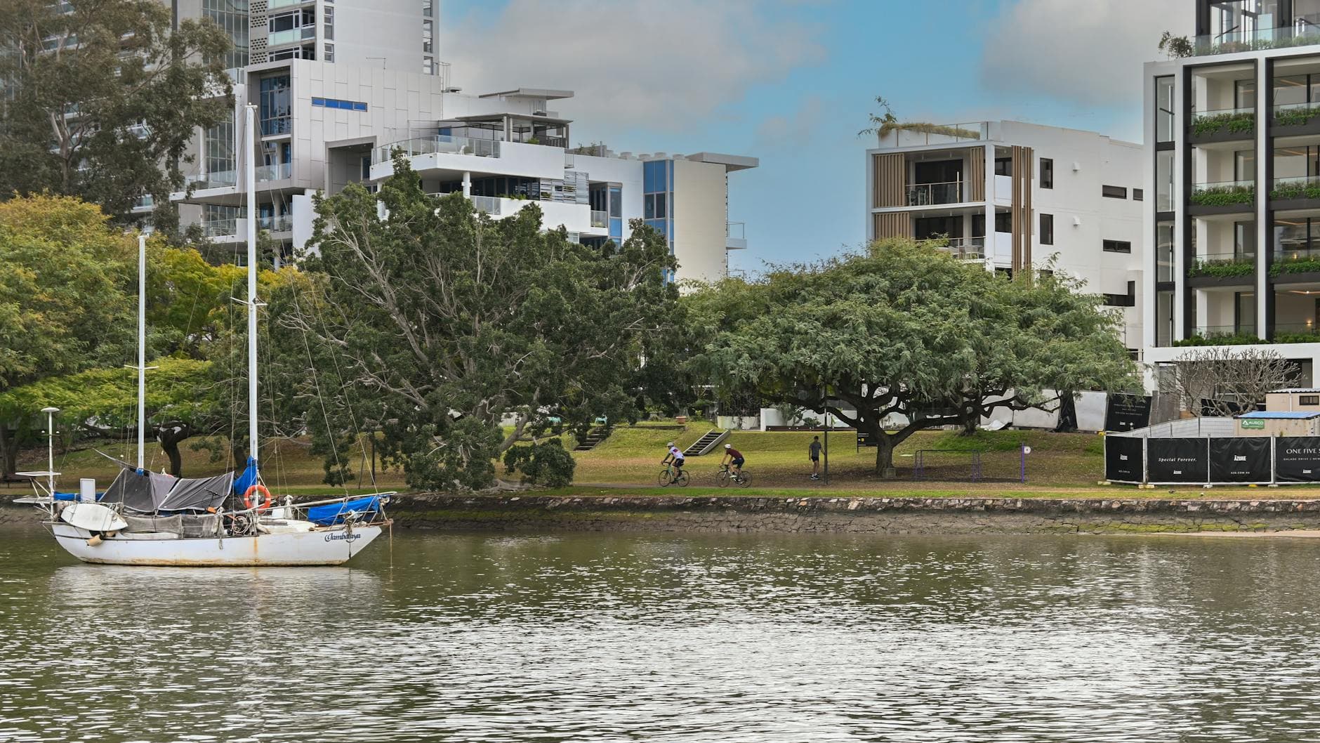 Boat docked in Brisbane with modern buildings and lush trees lining the riverbank.