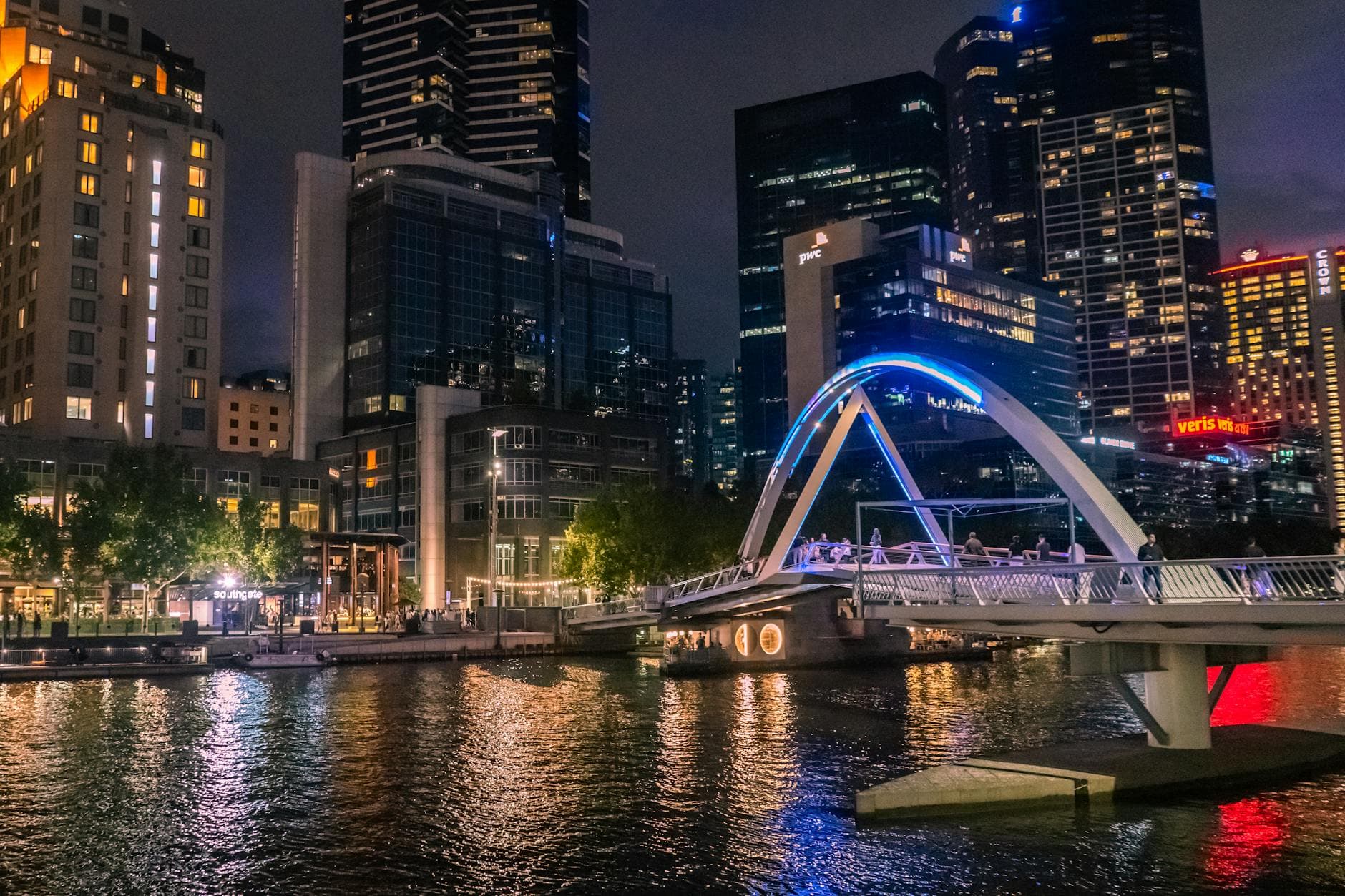 Illuminated Evan Walker Bridge crossing Yarra River in Melbourne's skyline at night.