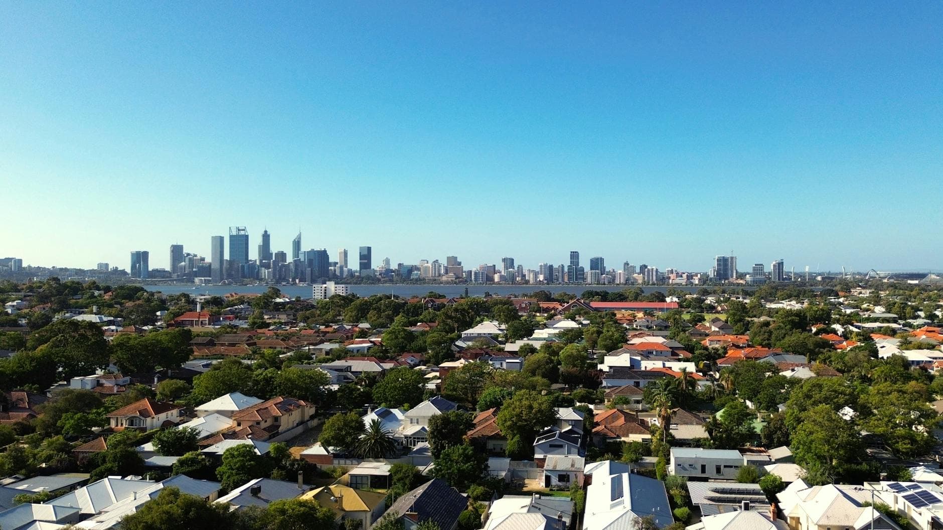 Stunning aerial view of Perth city skyline and suburban homes under clear blue sky.