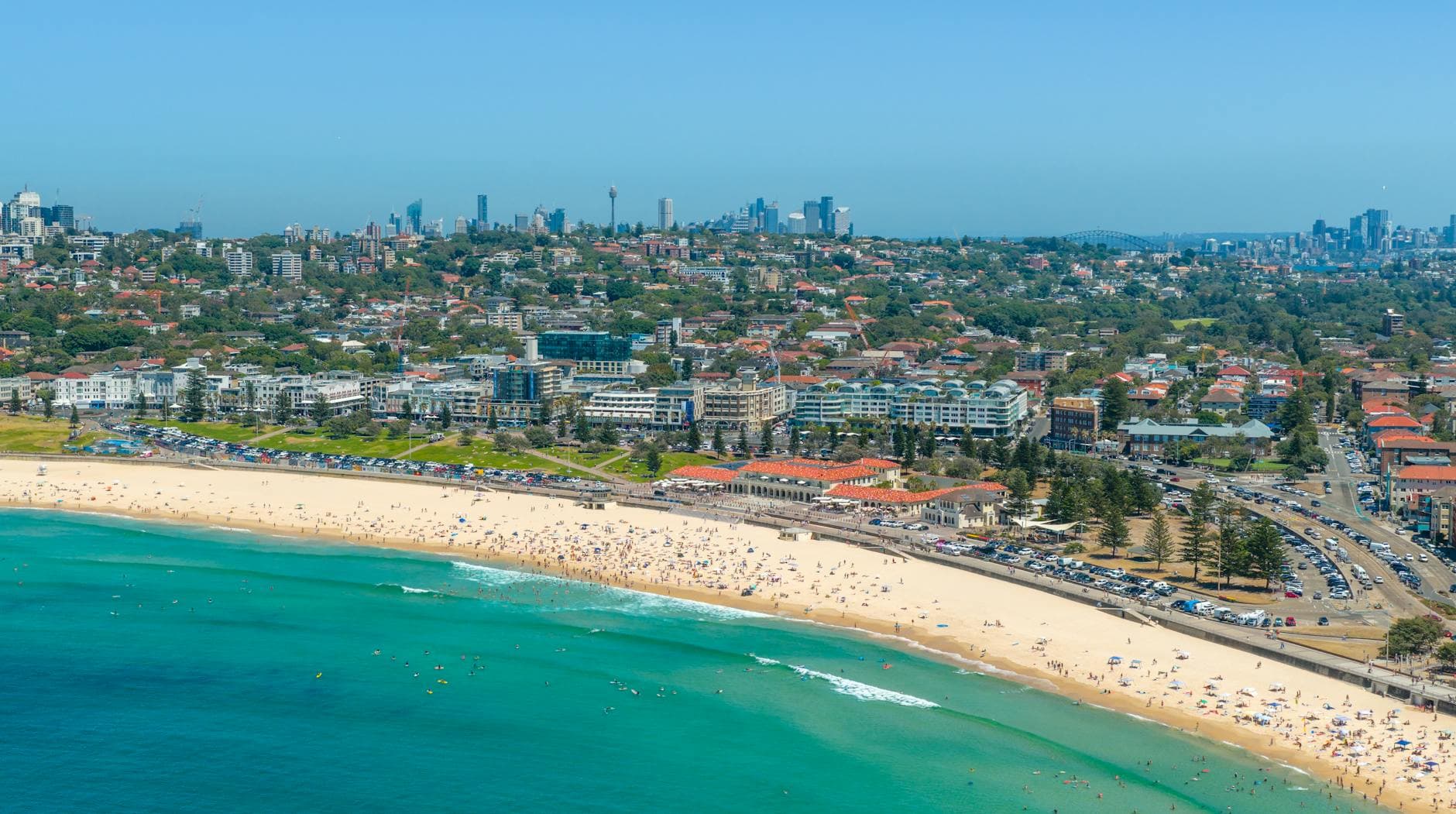 Capture the vibrant coastal scene of Bondi Beach in Sydney from above, showcasing city skyline and sandy shores.