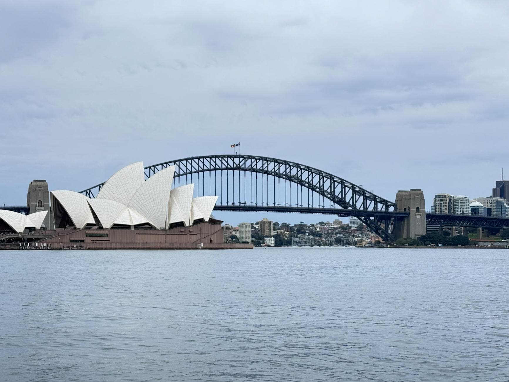 Scenic view of Sydney Opera House and Harbour Bridge on a cloudy day.