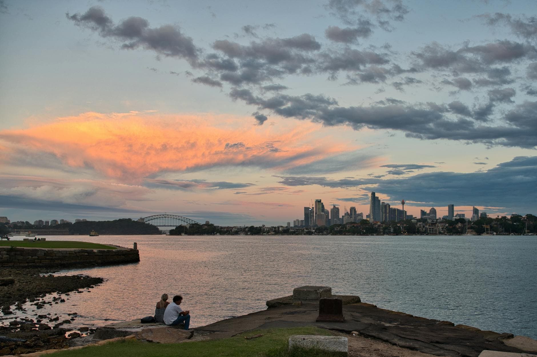 Scenic view of Sydney Harbour Bridge and skyline during a vibrant sunset with clouds.
