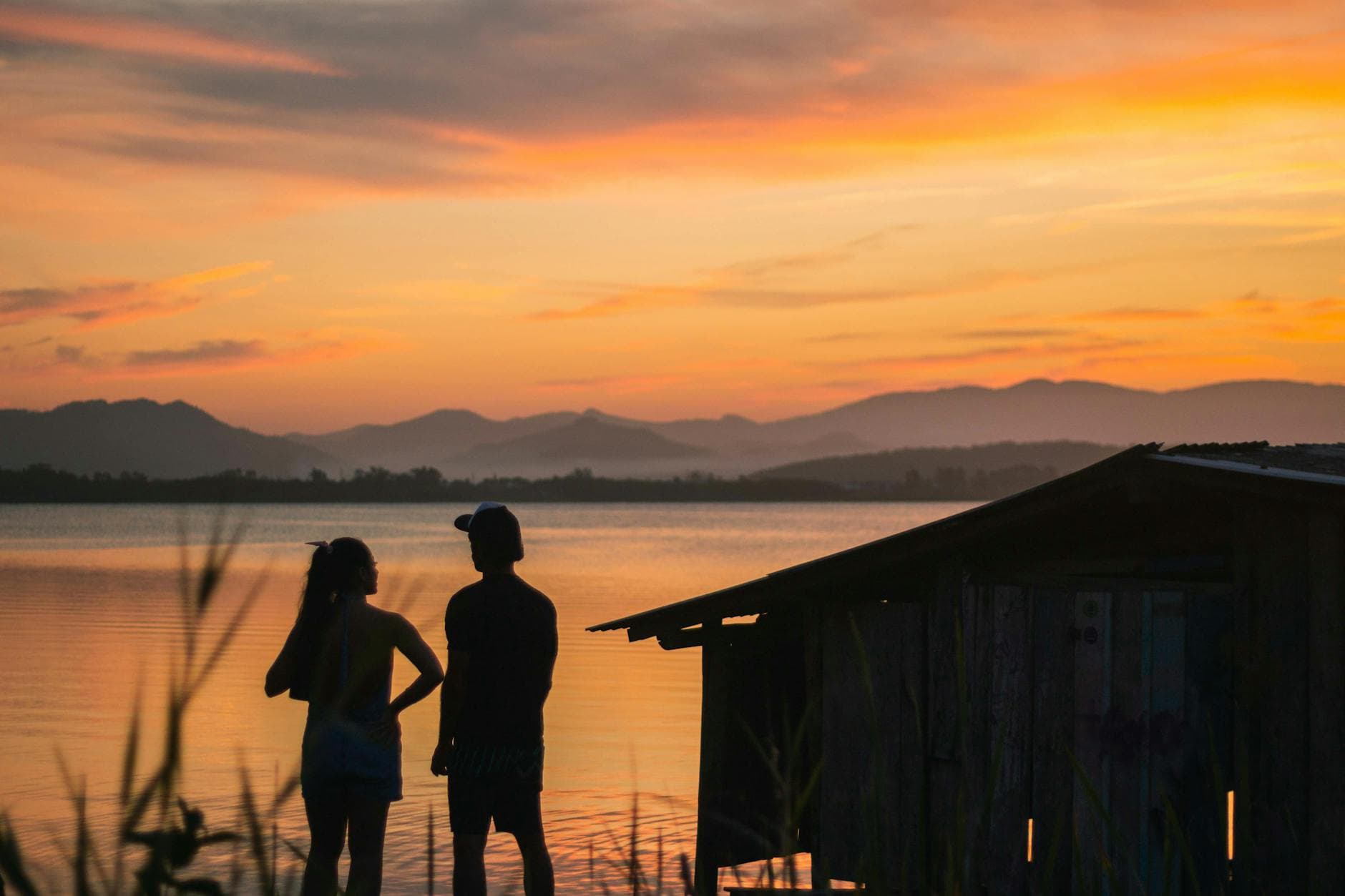 Romantic silhouette of a couple by a lake during a vibrant sunset, capturing the beauty of the golden hour.