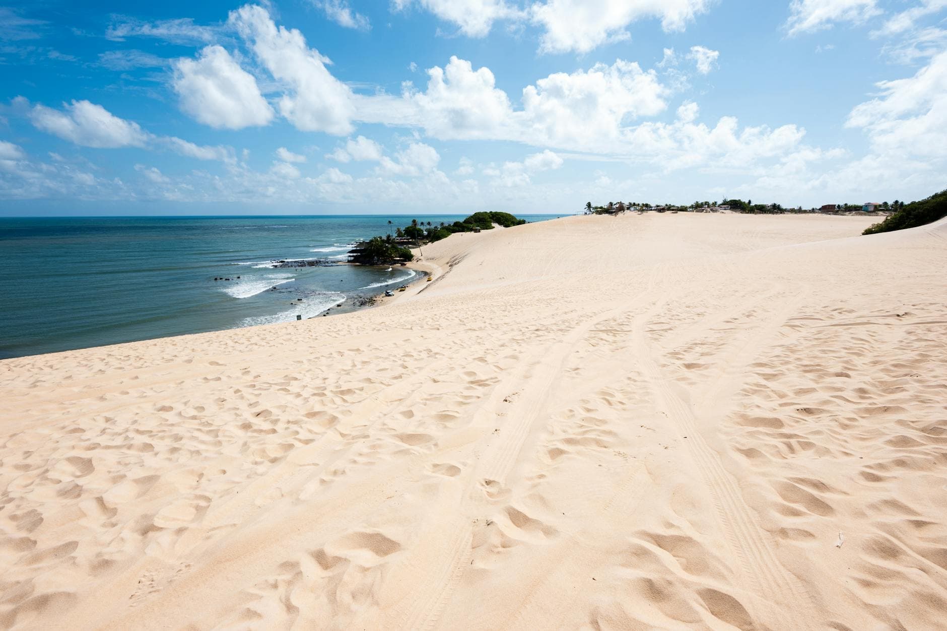 Expansive sand dunes leading to the ocean under a bright blue sky in Natal, Brazil.