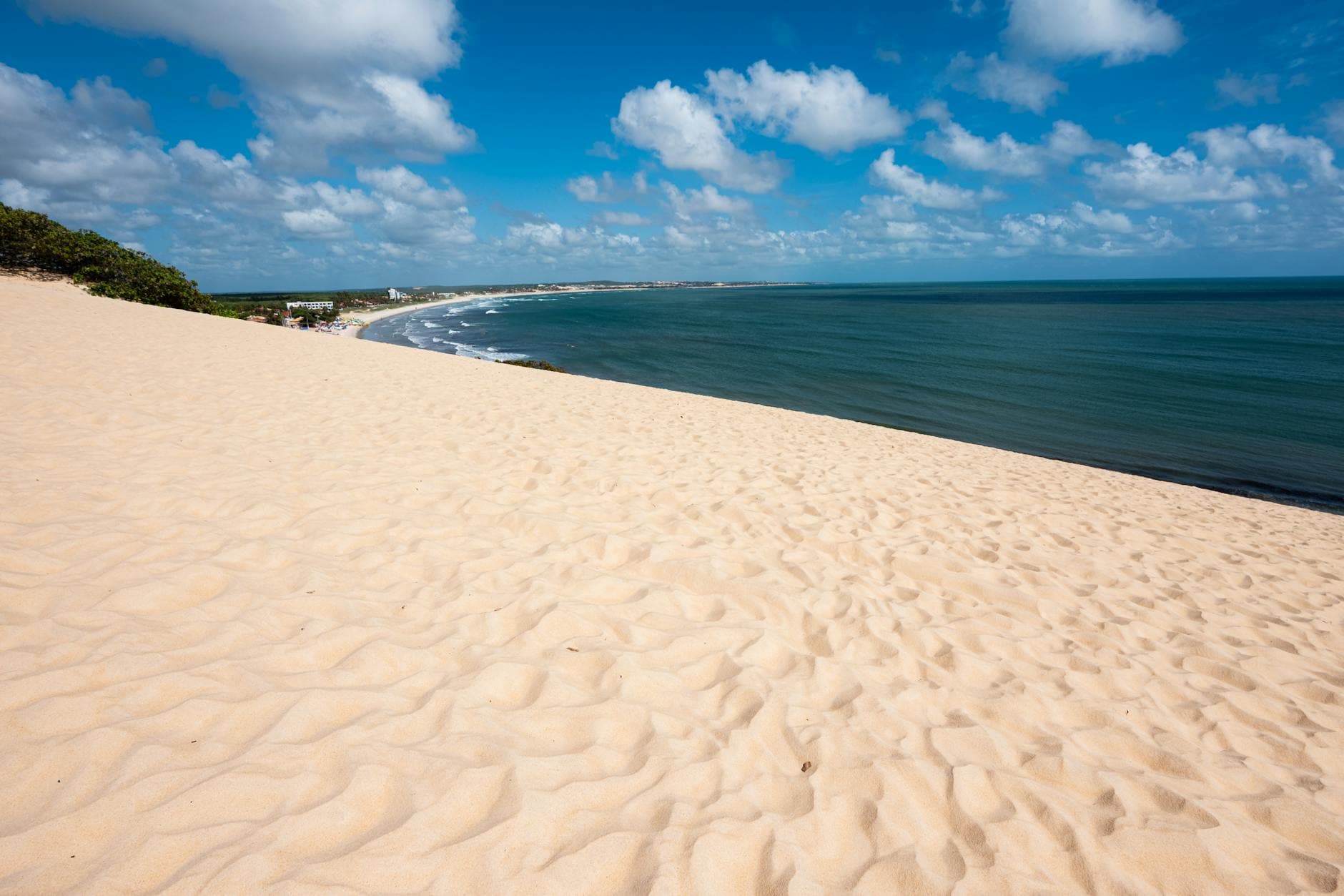Expansive sand dunes with a breathtaking view of the beach in Natal, Brazil under a bright blue sky.