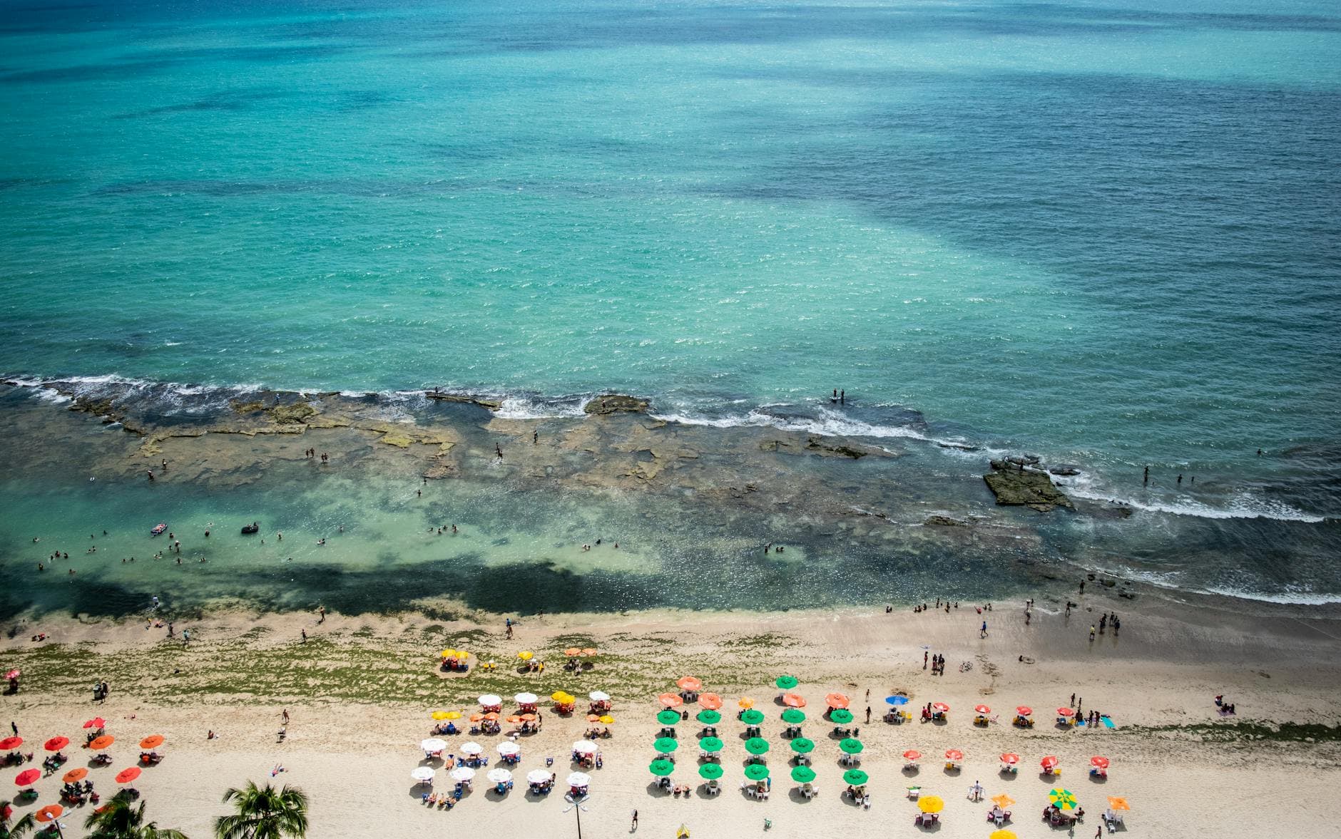 Discover the vibrant beachfront of Recife with colorful umbrellas and turquoise waters from above.