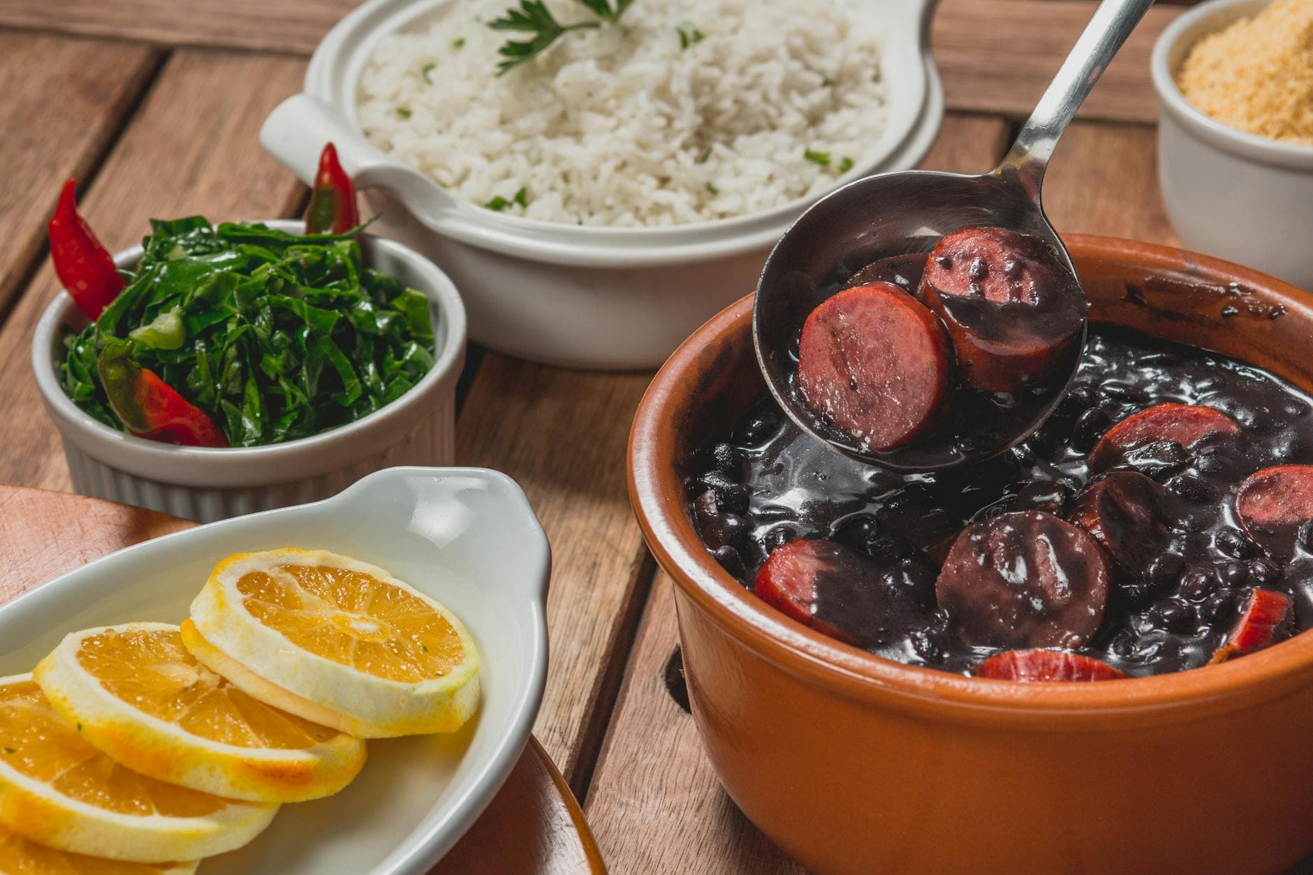 Delicious Brazilian feijoada with rice, greens, and orange slices served on a wooden table.