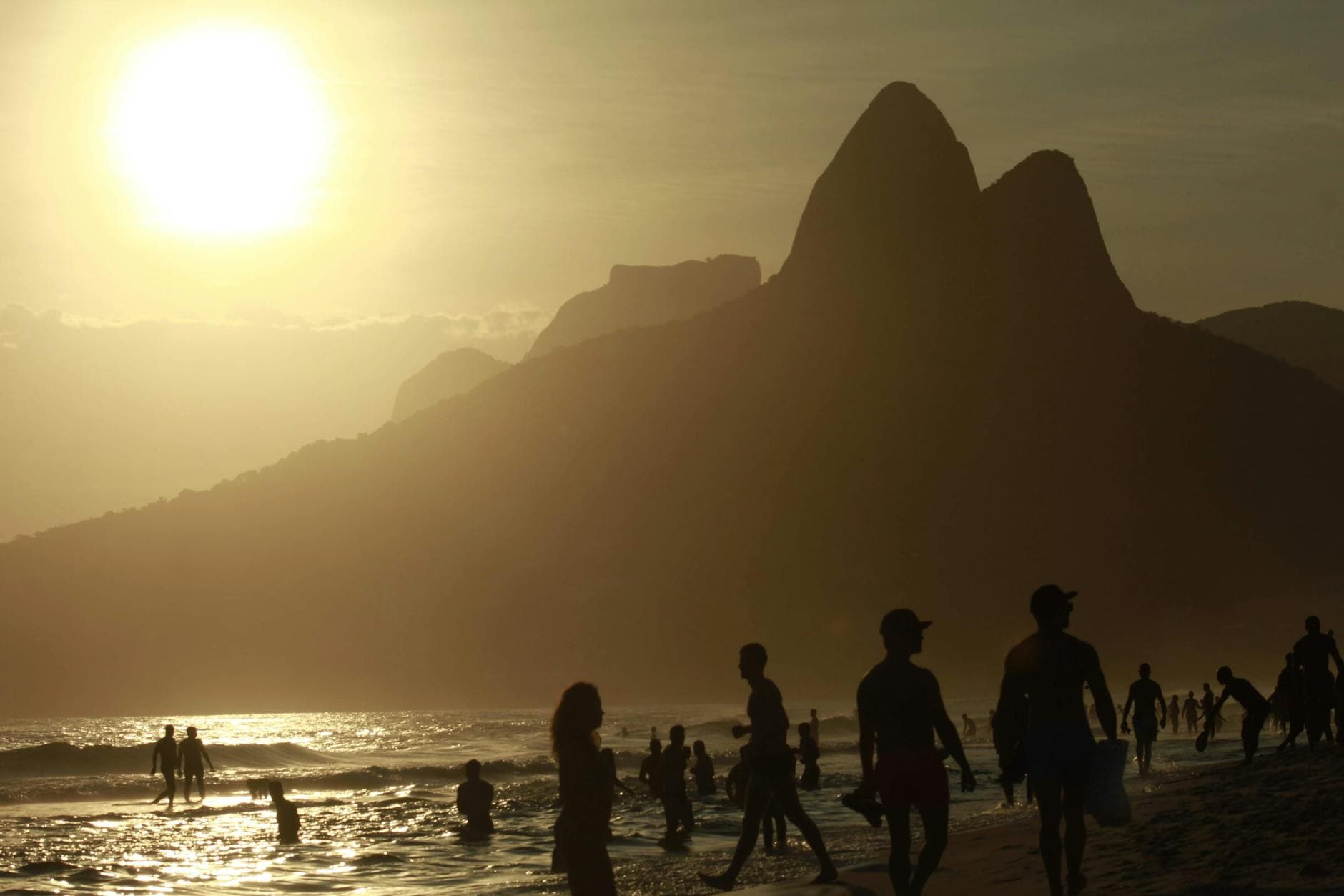 Silhouettes of people enjoying the beach at sunset with Rio's iconic mountains in the background.