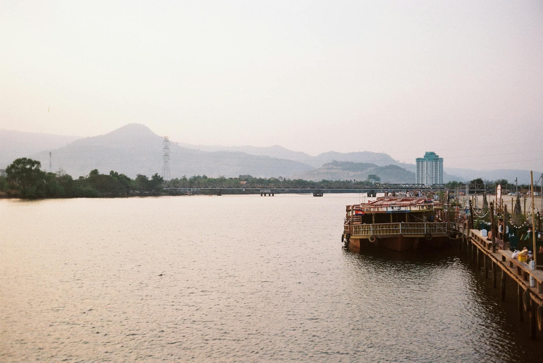 A tranquil view of a river in Kampot, Cambodia at dusk, capturing boats and distant mountains.