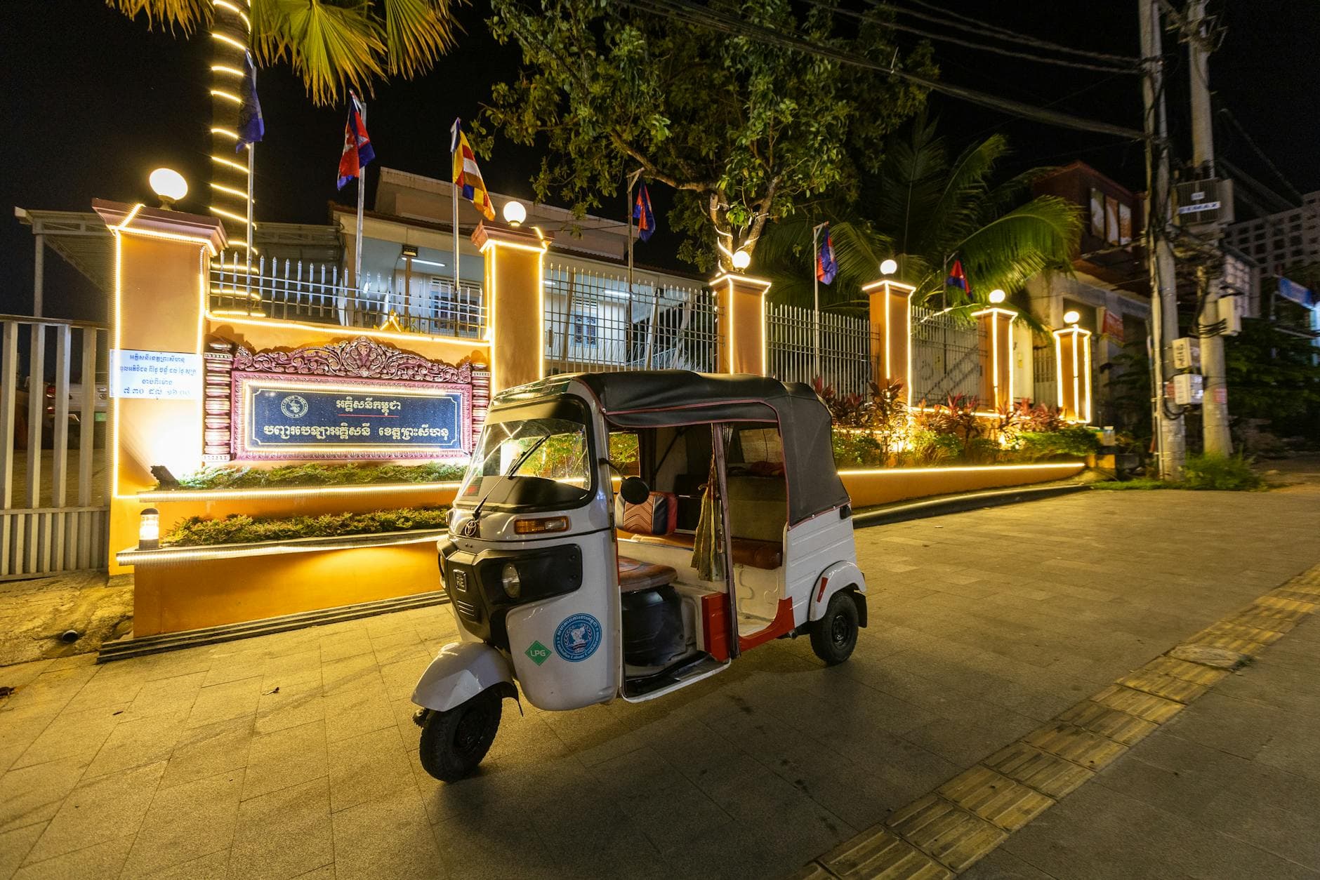 A parked tuk-tuk in front of a lit building at night in Cambodia, showcasing vibrant urban nightlife.