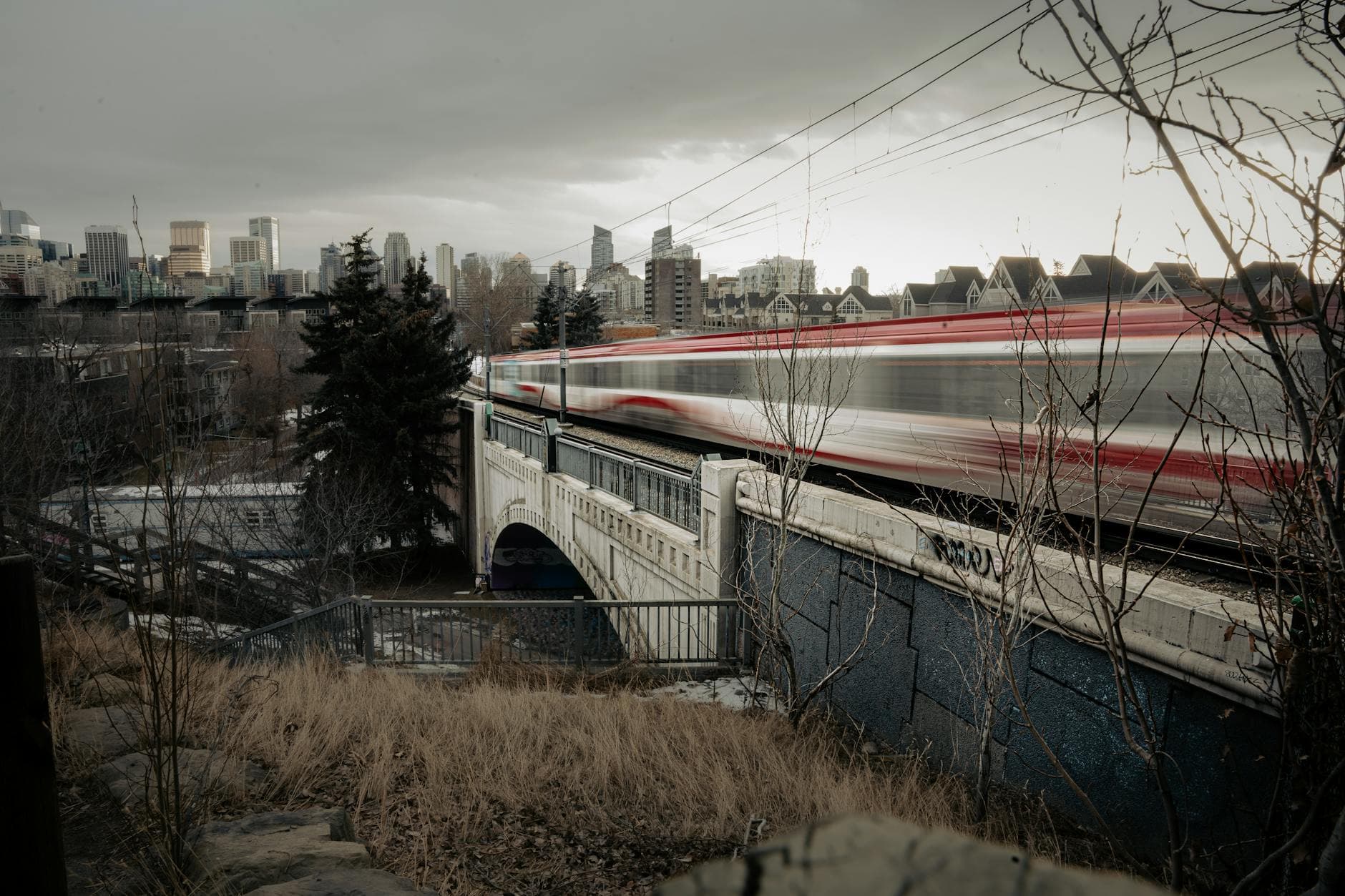 A high-speed train speeding across a bridge in Calgary with city skyline in the background.