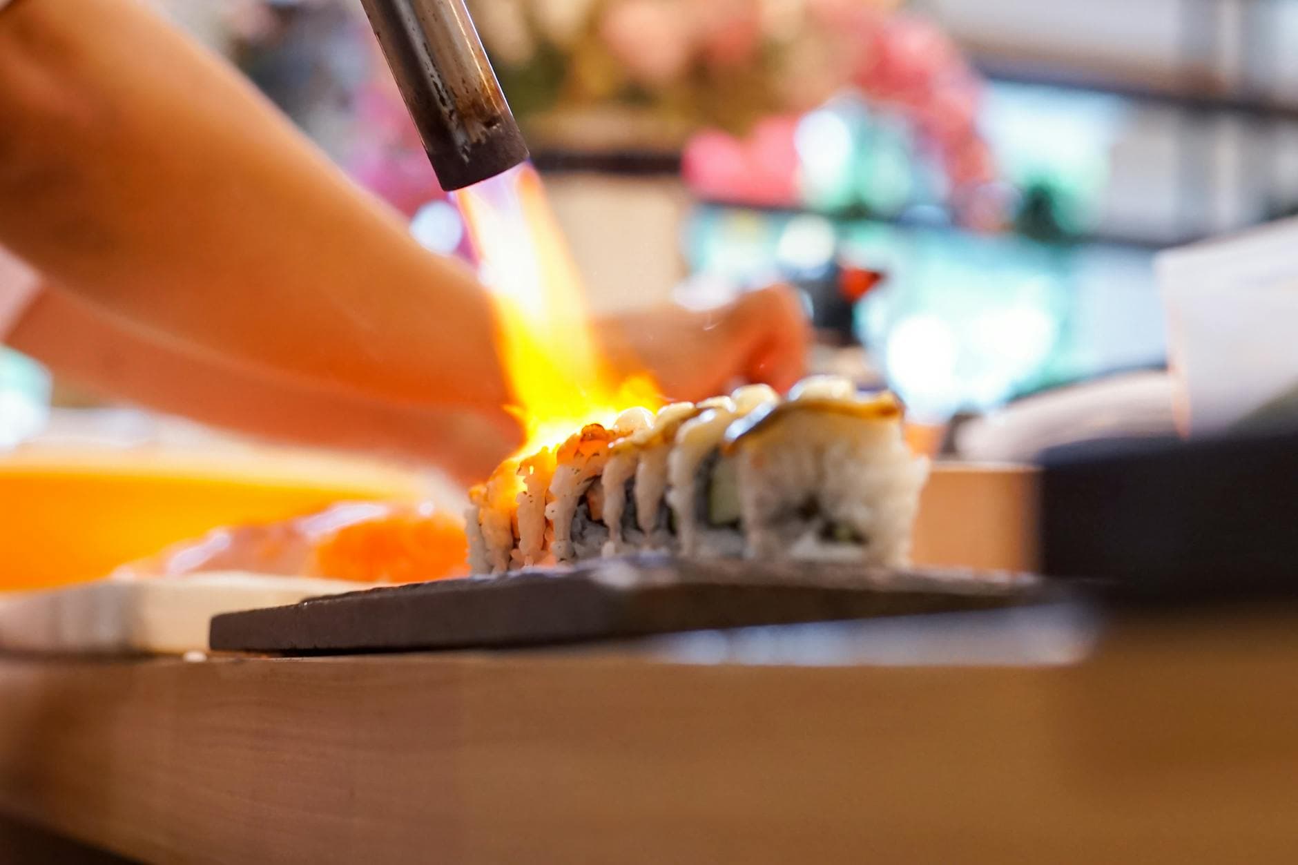 Close-up of sushi being torched by a chef for a crispy finish, highlighting Japanese cuisine preparation.