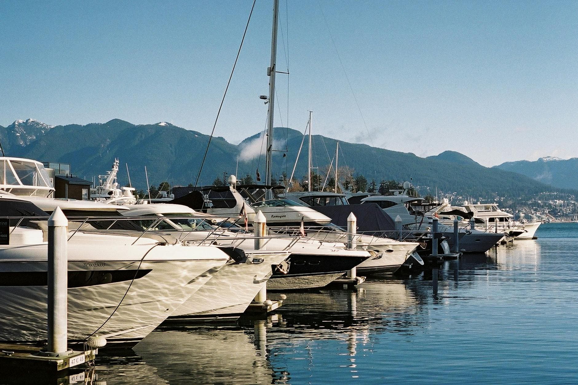 Discover tranquility at Vancouver's Coal Harbour with yachts and mountain views reflecting in calm waters.