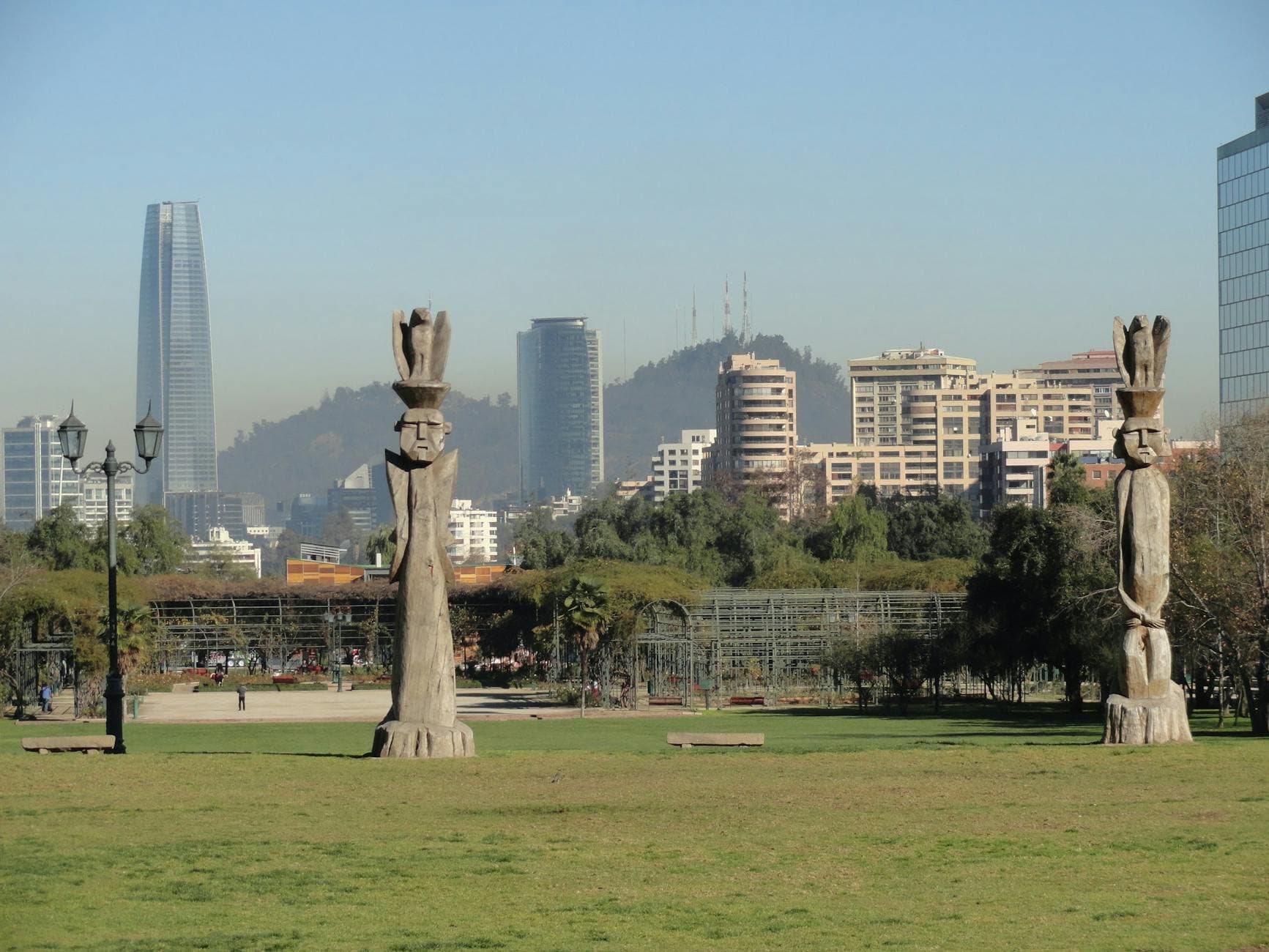 View of Santiago skyline from a green plaza featuring Totem poles and modern skyscrapers.