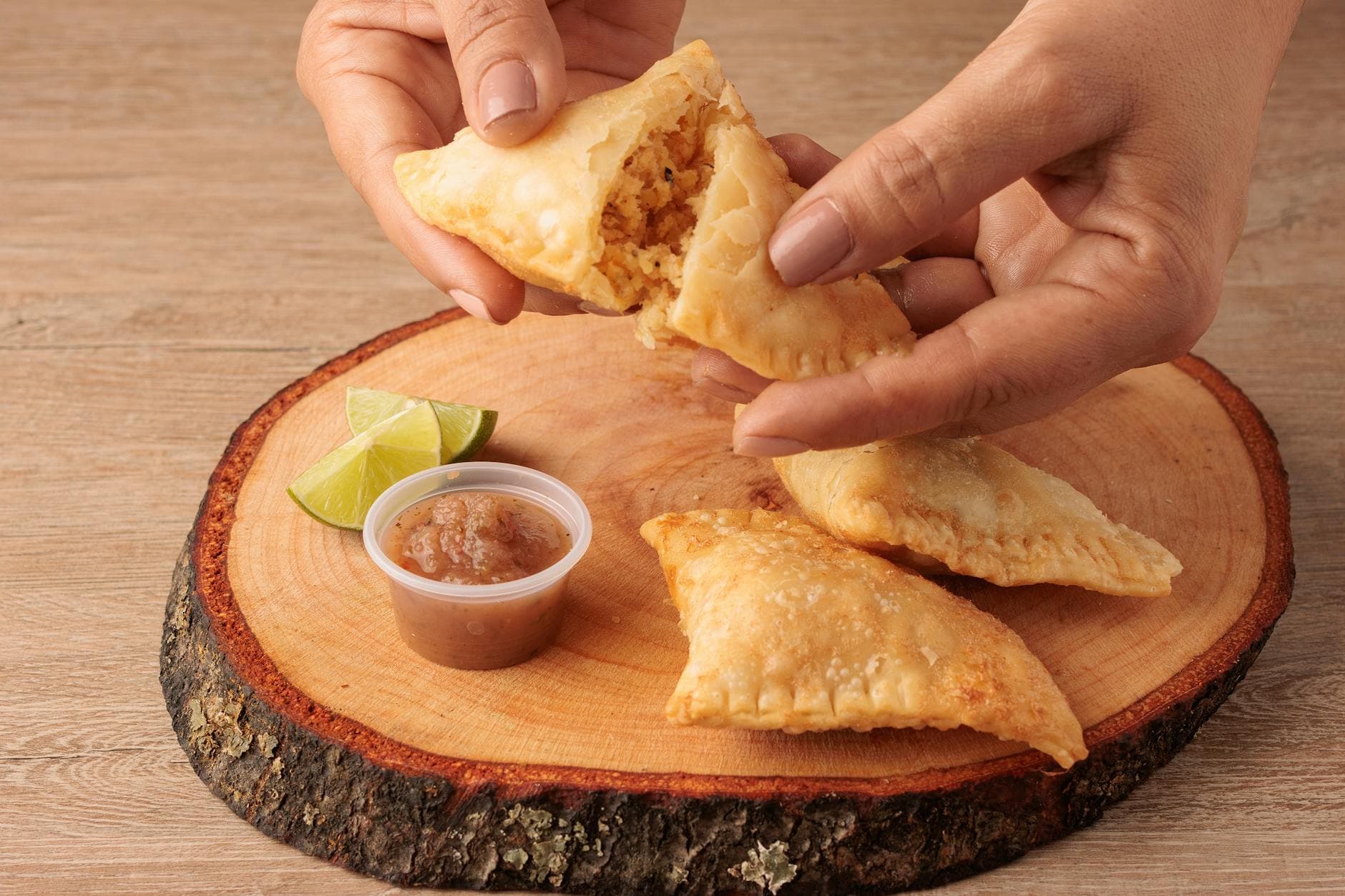 Colombian empanadas with tangy salsa and lime slices on a wooden platter.