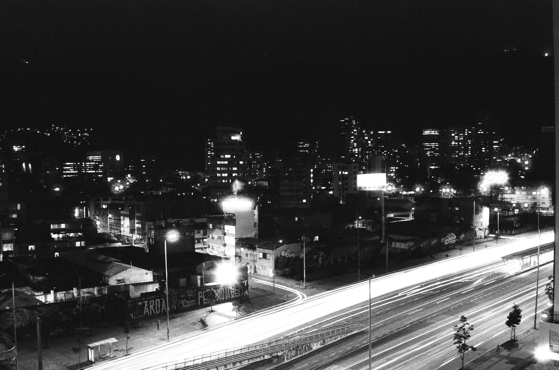 Black and white cityscape of Bogotá at night with light trails and skyline.