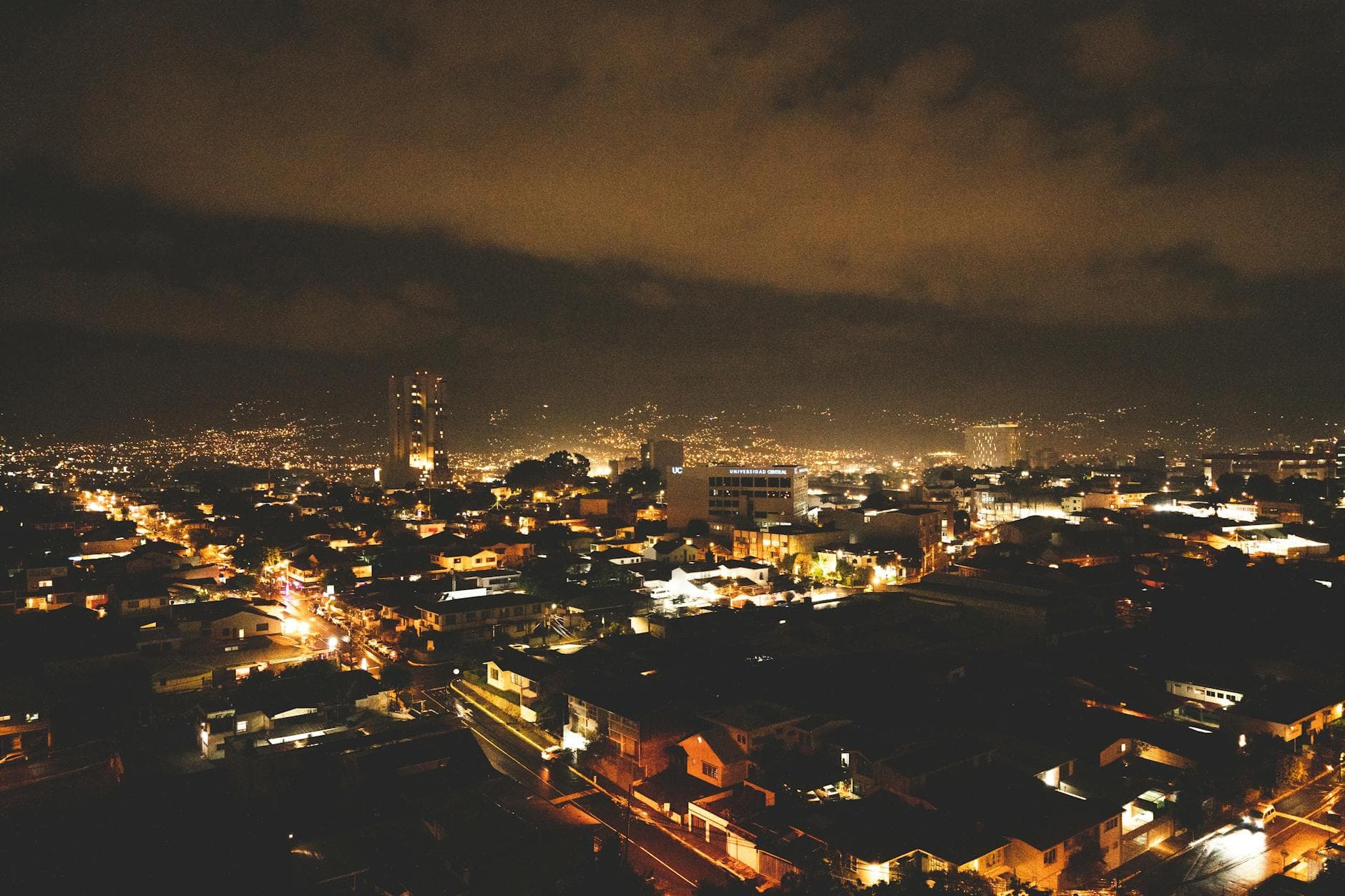 A breathtaking cityscape at night with illuminated buildings and twinkling city lights under a dramatic sky.