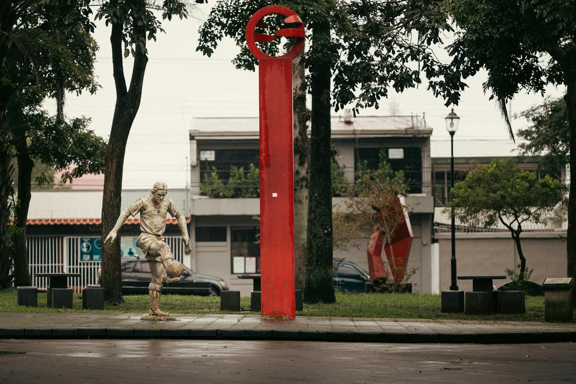 A stone statue of a soccer player beside a red column in Alajuela, Costa Rica park.