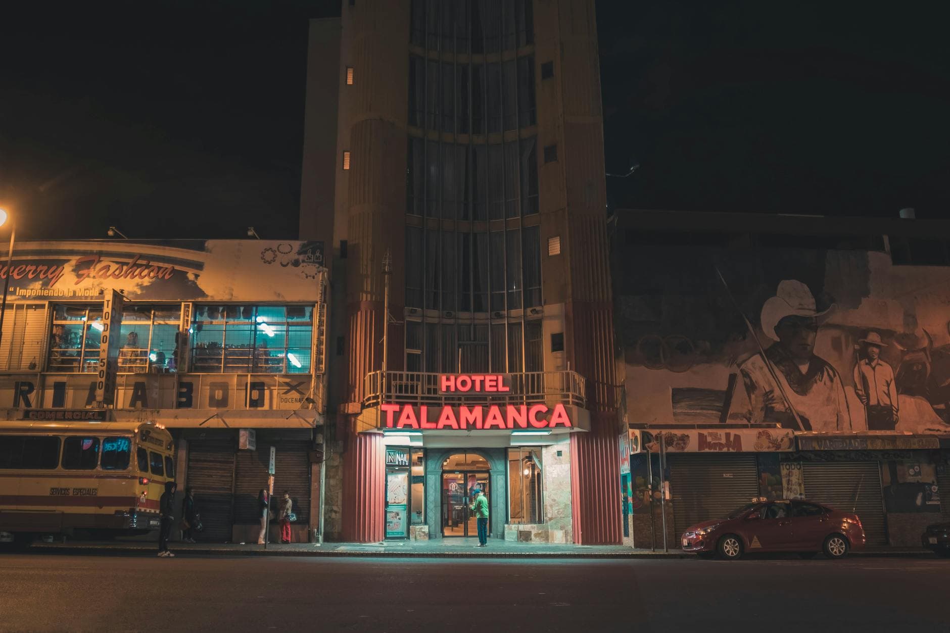 Urban night view of Hotel Talamanca with neon lights, street activity, and striking murals.