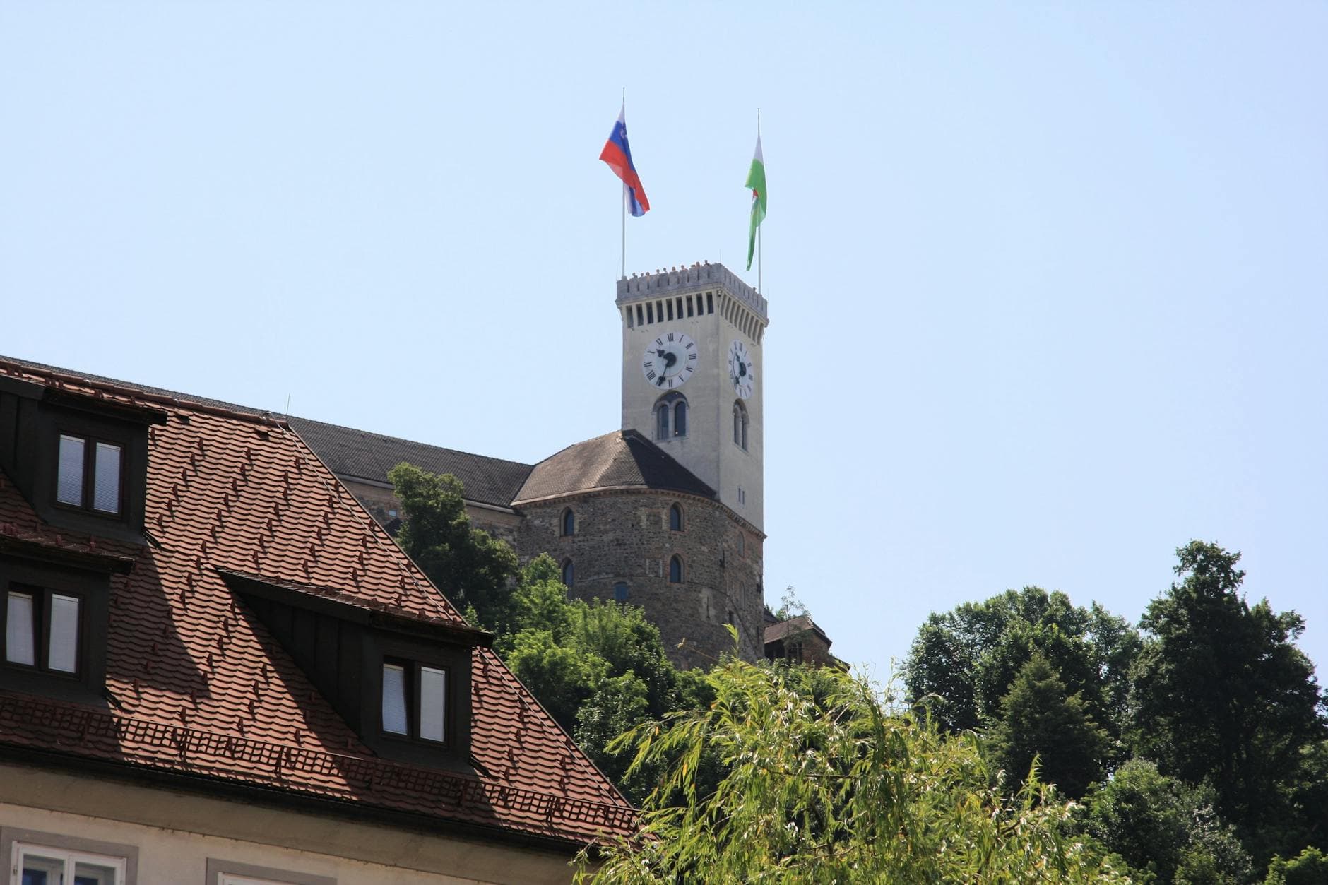A captivating view of Ljubljana Castle with Slovenian flags under a clear summer sky.
