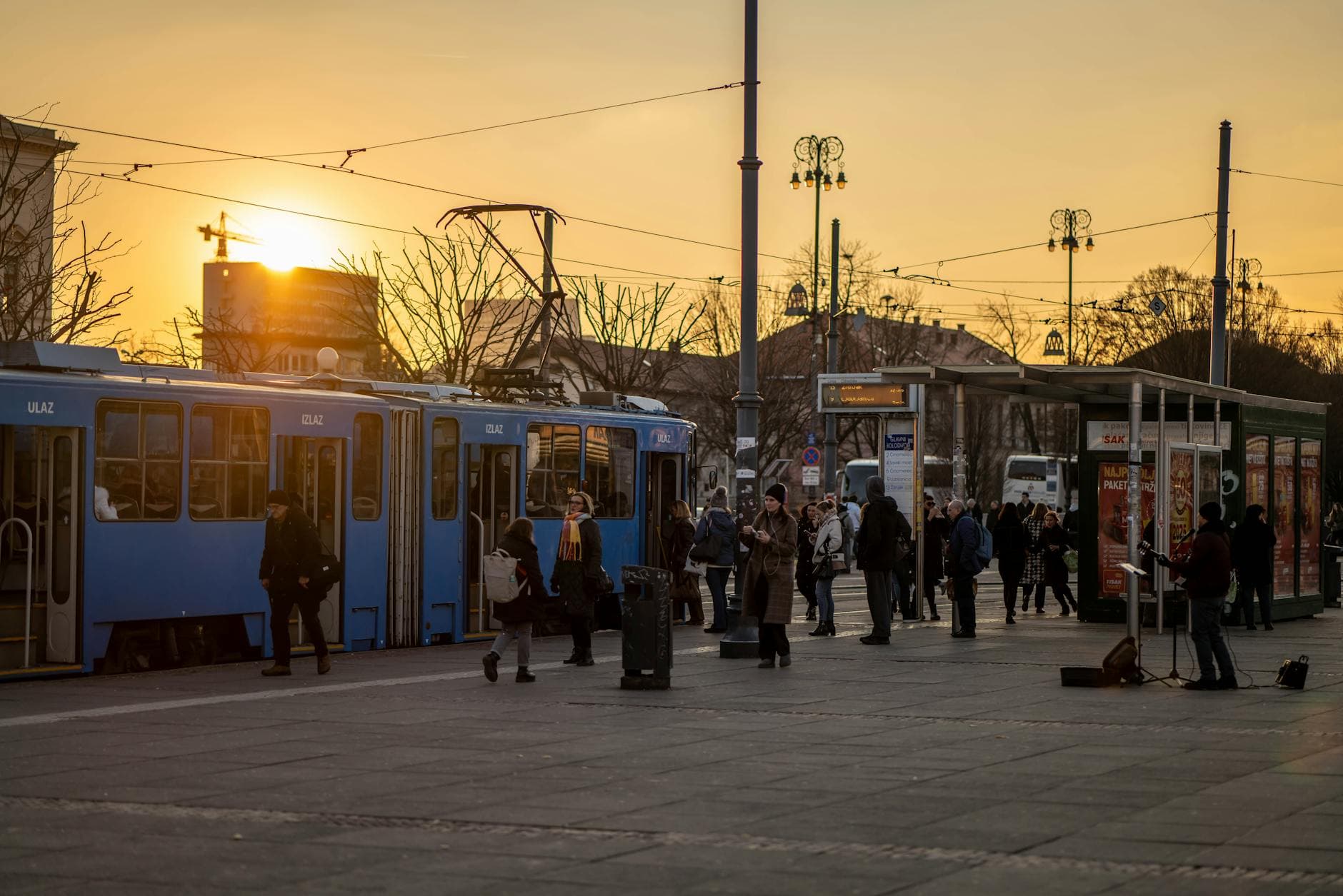 People boarding trams during sunset in Zagreb, creating a vibrant urban scene with warm tones.