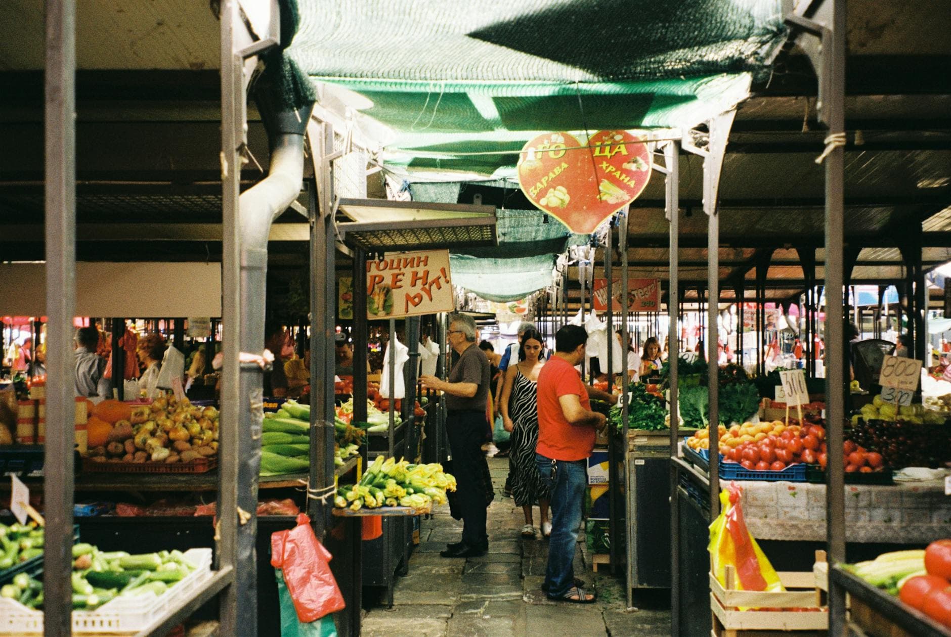 A bustling outdoor farmer's market with fresh vegetables and people shopping on a sunny day.