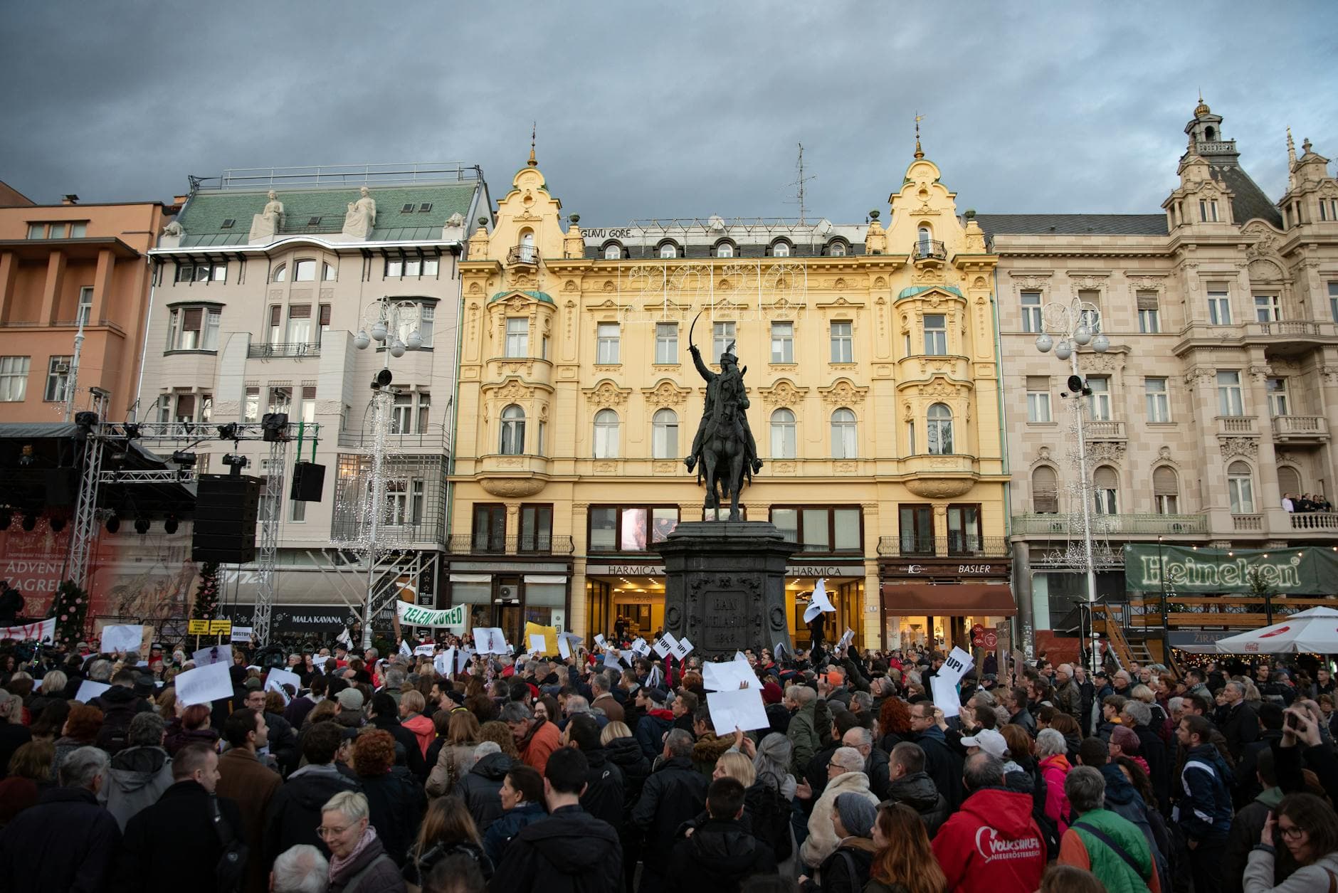 A crowd gathers for a protest at Ban Jelačić Square in Zagreb, Croatia, under a cloudy sky.