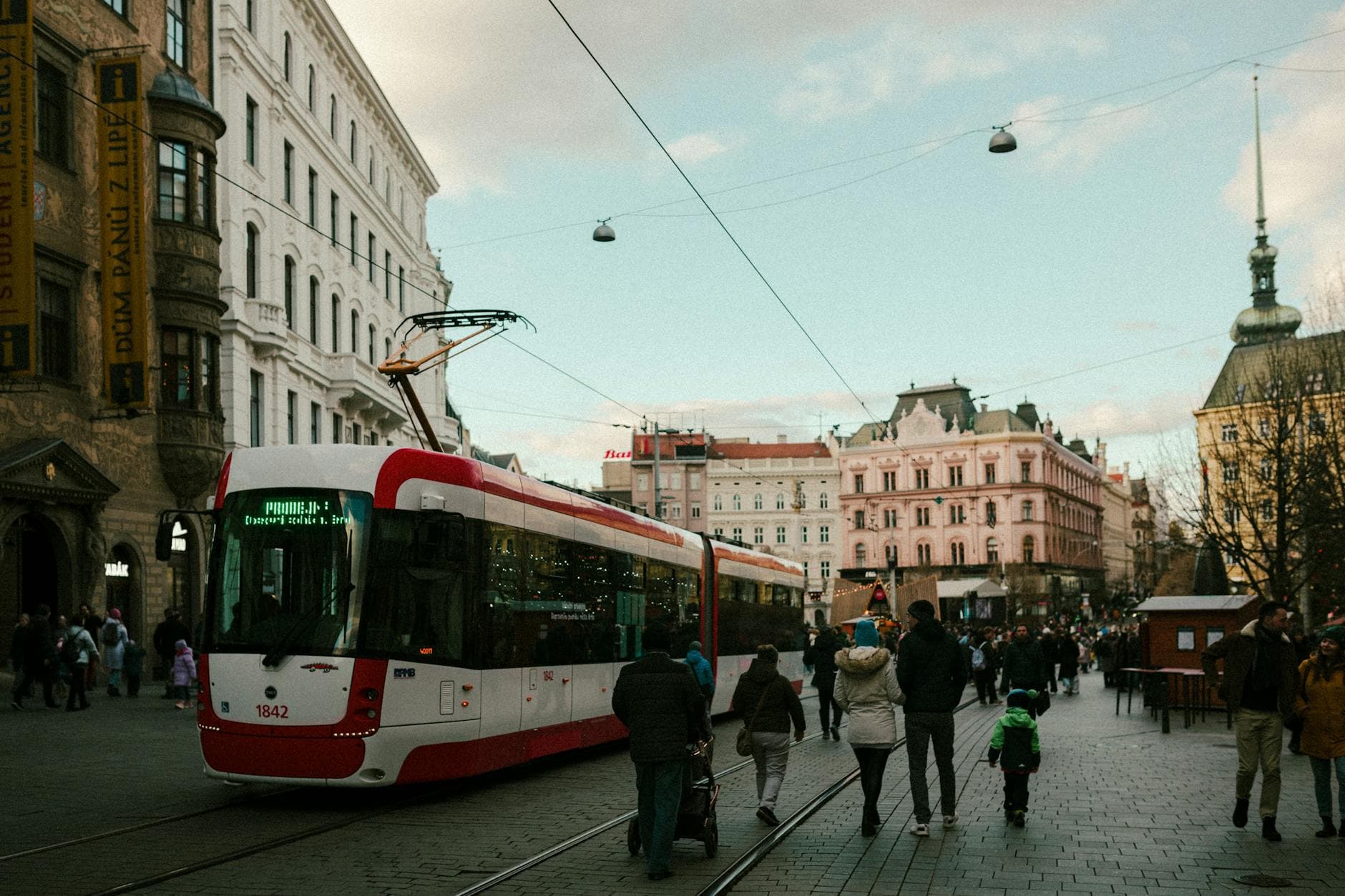 Busy street with a red streetcar and pedestrians in a historic European city center.