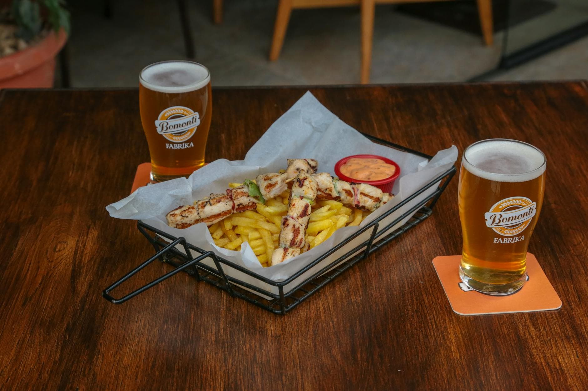 A casual dining setup with beer, grilled skewers, and fries served indoors.