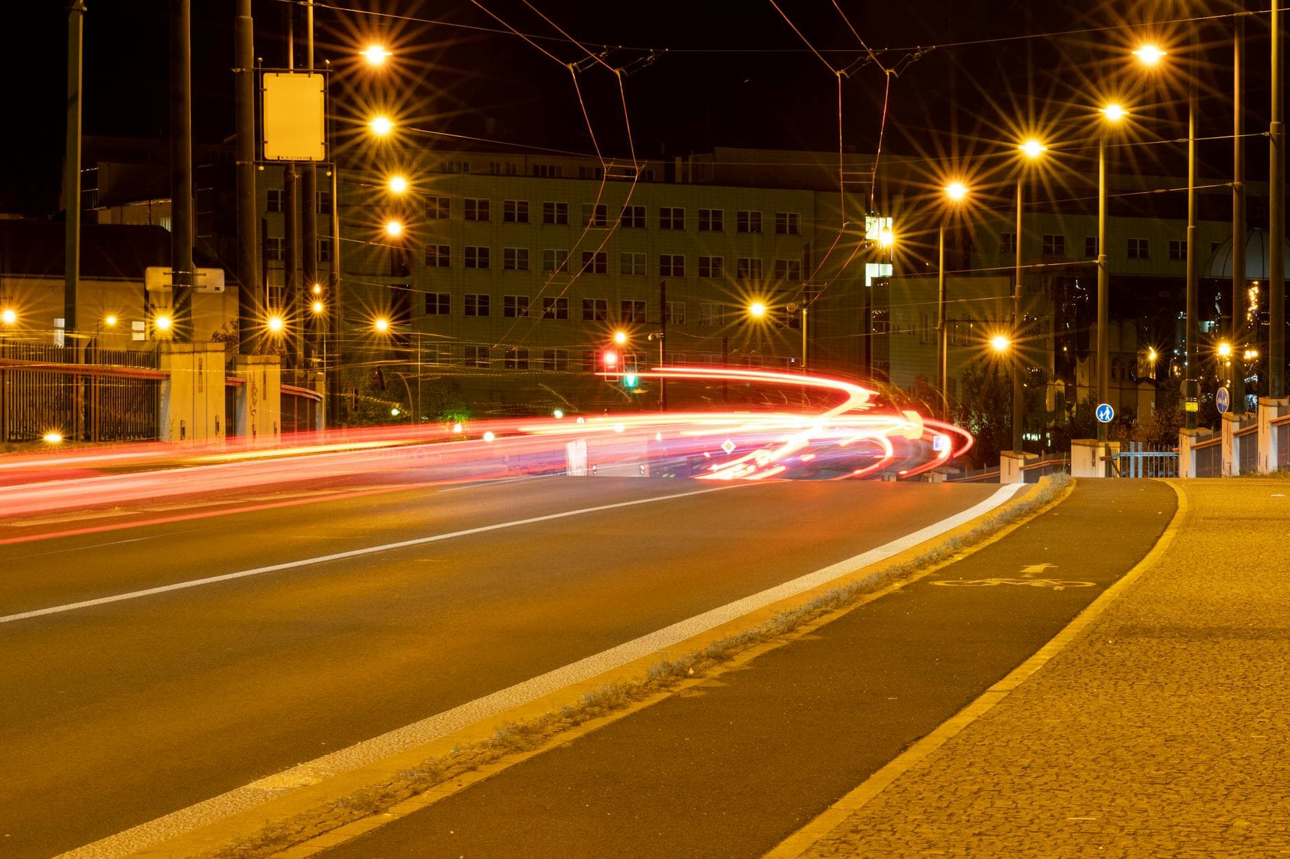 Captured in Plzeň, this night scene features vibrant car light trails and street lights on a quiet city street.