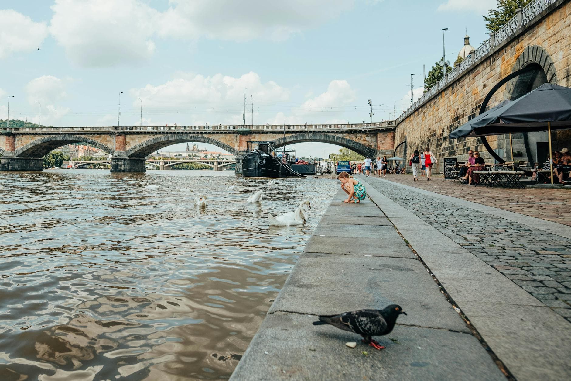Explore the picturesque Vltava riverfront with the iconic Palacky Bridge in Prague, vibrant with urban life.