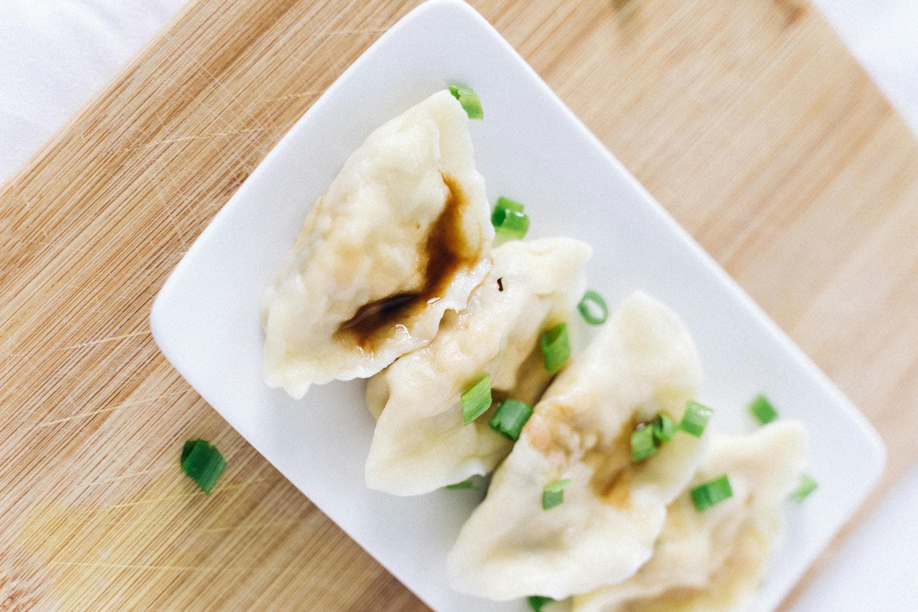 Delicious Chinese dumplings with soy sauce and chopped scallions on a plate.