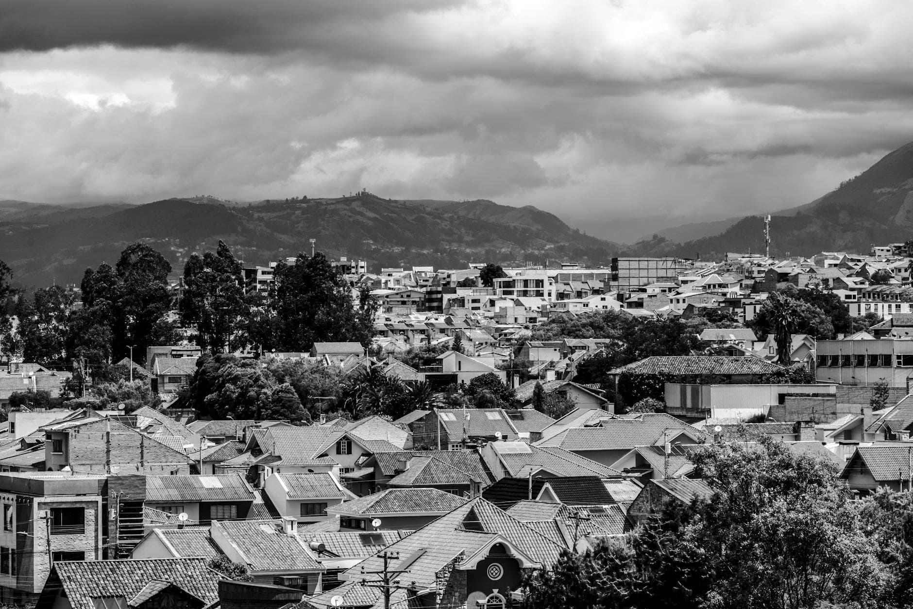 A dramatic black and white cityscape of Cuenca, Ecuador, showcasing the urban rooftops and distant mountains.
