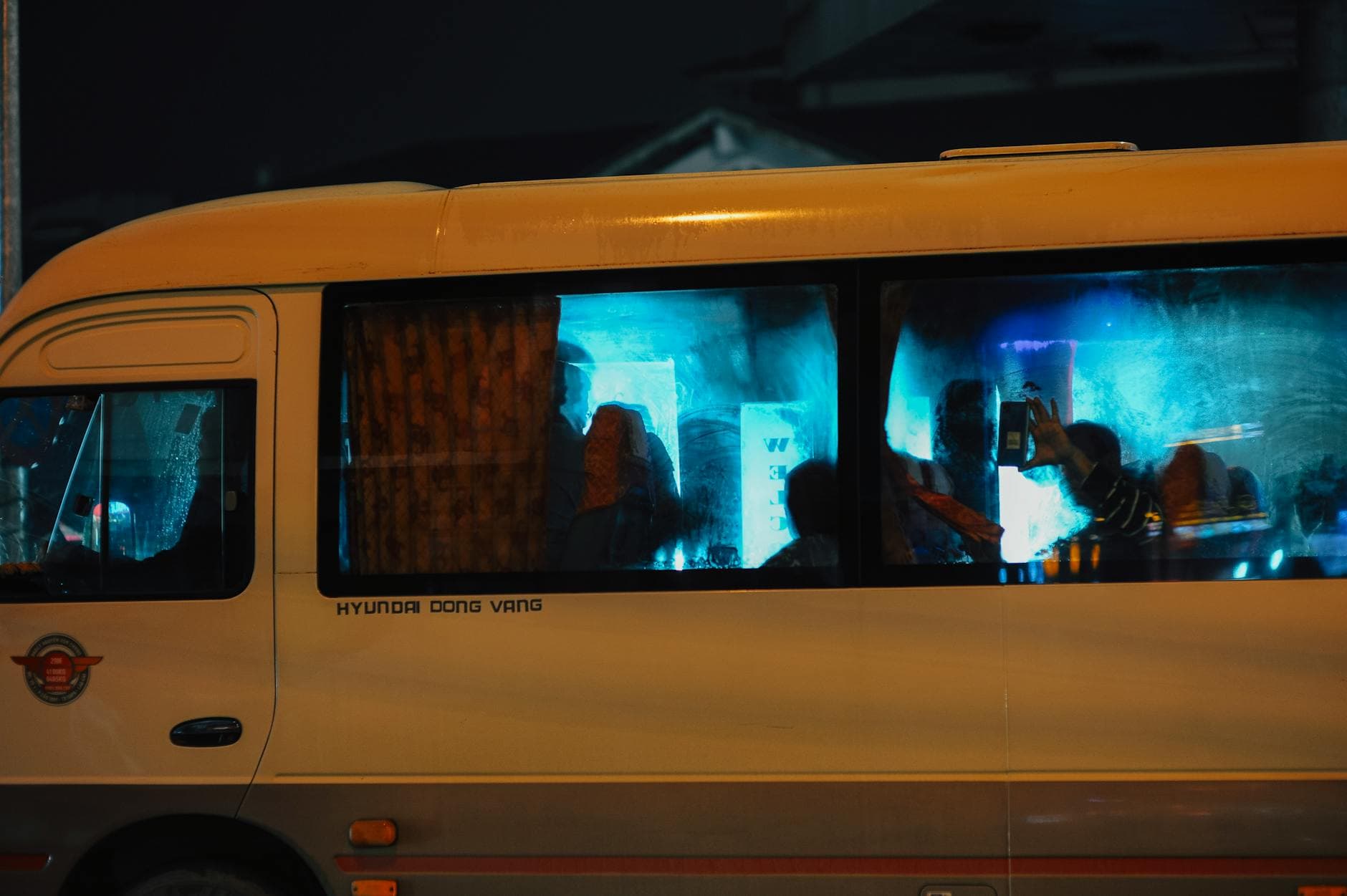 Silhouetted passengers on a bus at night with city lights reflecting on the windows.