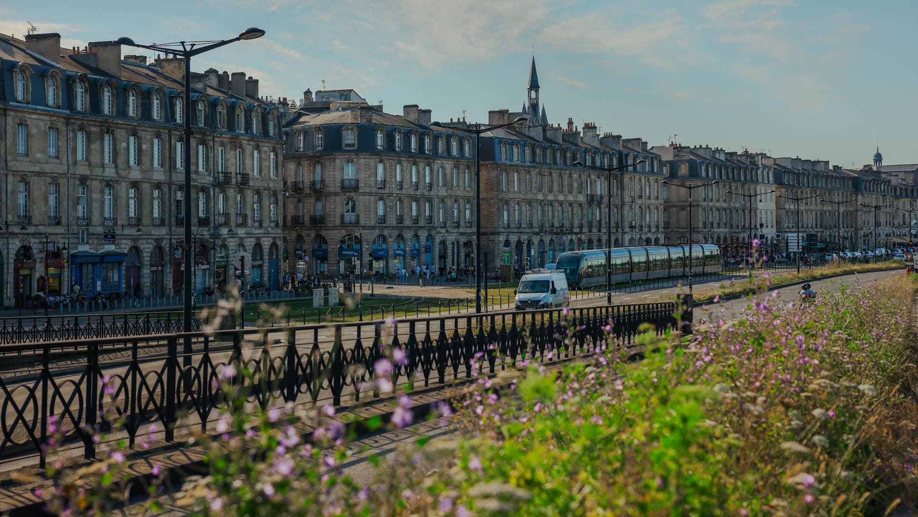 Charming view of historic buildings and tram in Bordeaux, France, with vibrant flowers in foreground.