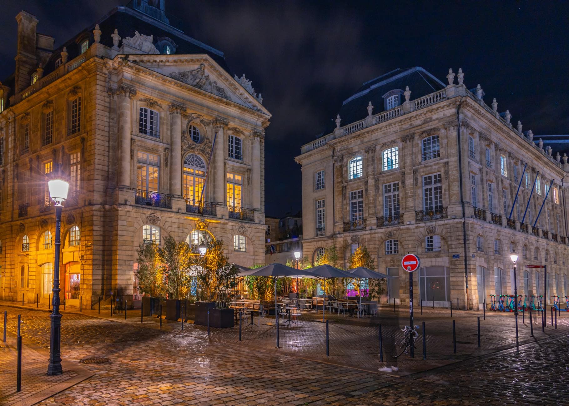 Night view of elegant historic buildings in a European plaza with streetlights and reflections.