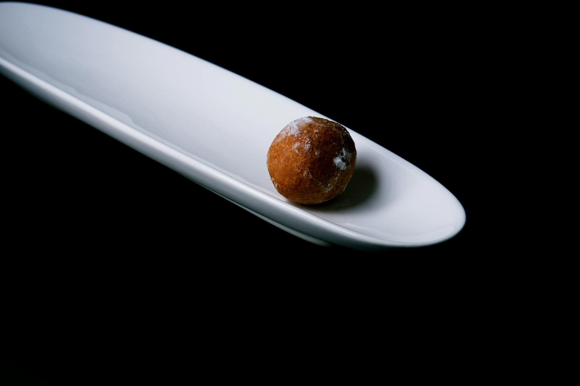 Minimalist image of a single sweet praline on a sleek white plate against a black backdrop.