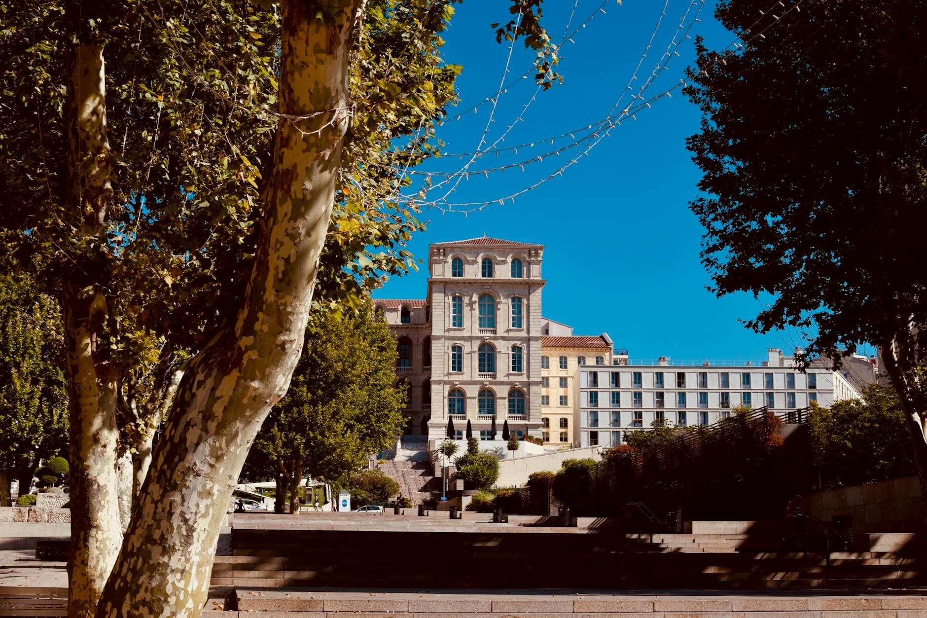 View of a historic architectural building in Marseille, surrounded by lush trees on a sunny day.