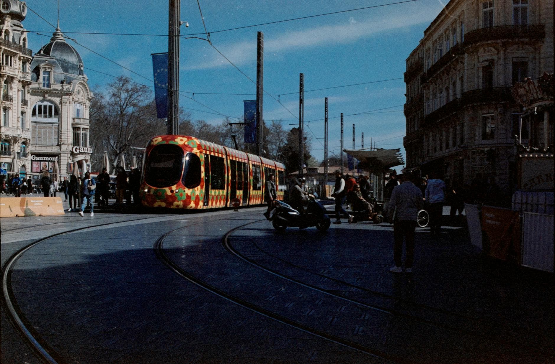 Colorful tram passing through a bustling street in Montpellier, France.