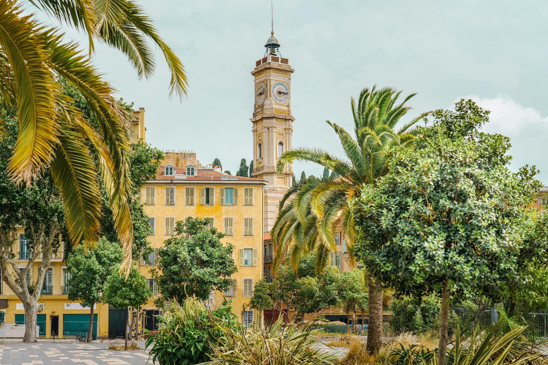 Beautiful clock tower and palm trees in sunny Nice, France, capturing a vibrant summer atmosphere.