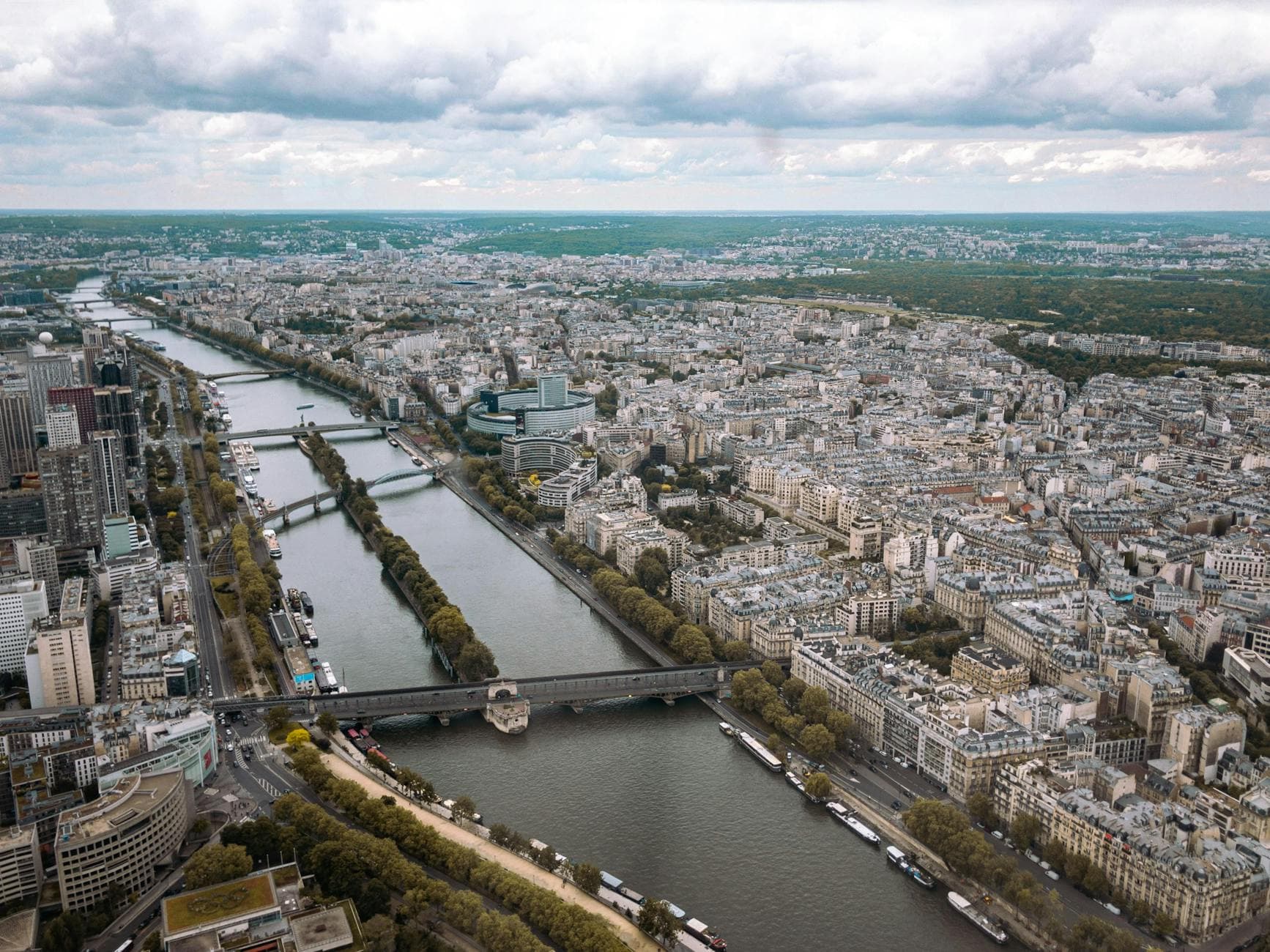 Stunning aerial view of Paris showcasing the Seine River and intricate cityscape under a cloudy sky.