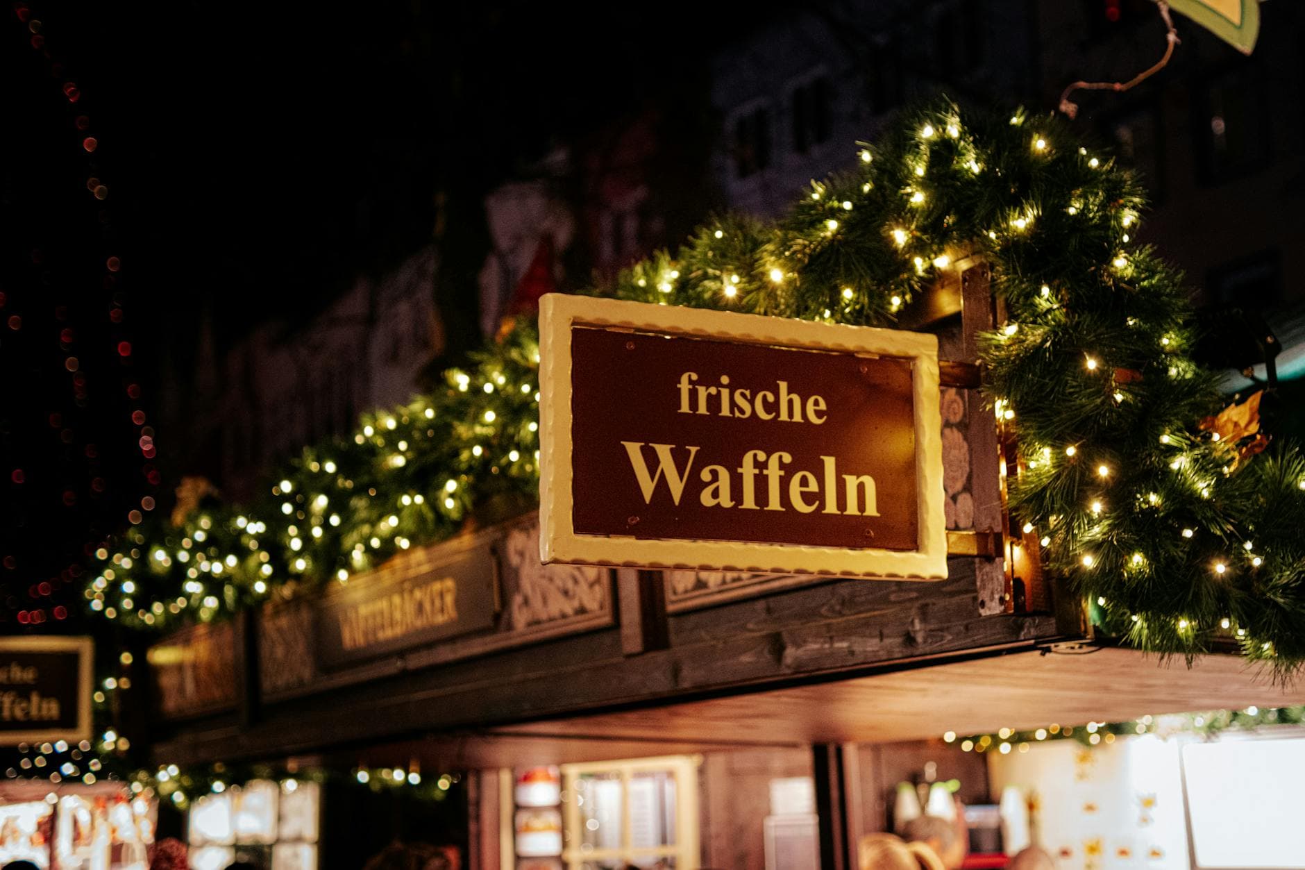Festive Christmas market stall serving waffles in Cologne, Germany with holiday lights and decor.