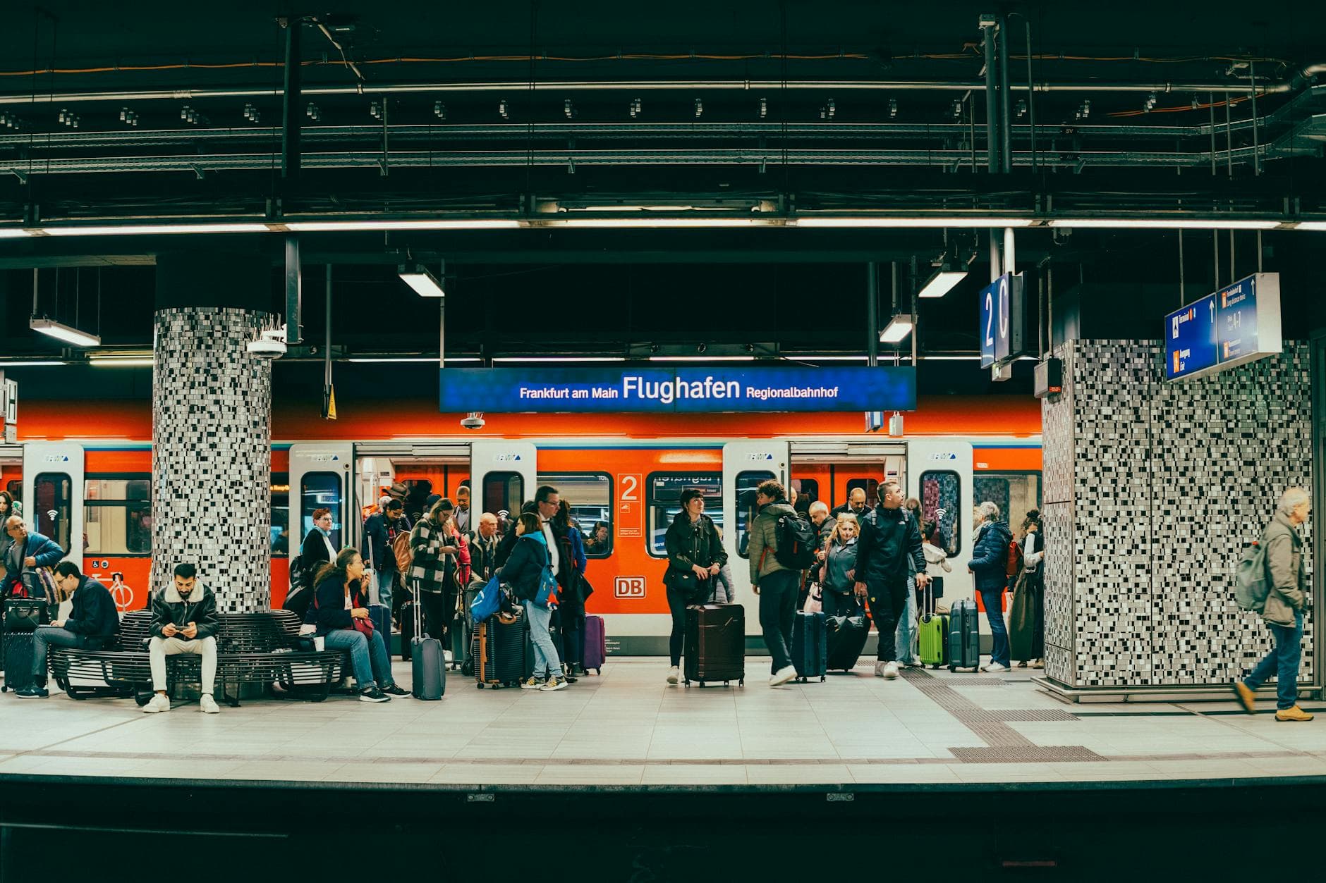 Passengers wait on the platform at Frankfurt am Main Flughafen train station with a regional train in the background.