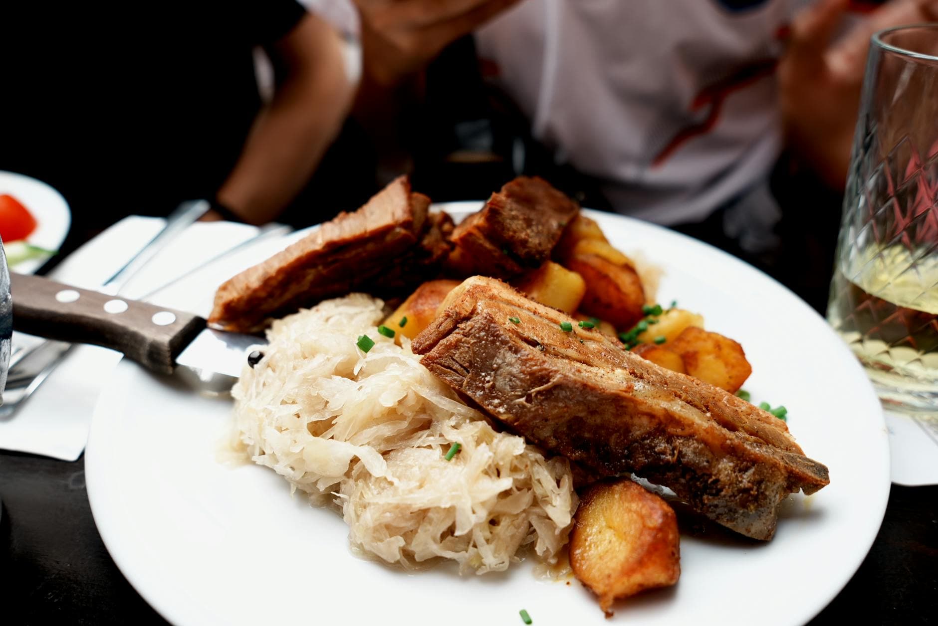 Plate of roast pork ribs, sauerkraut, and potatoes served in a cozy setting.