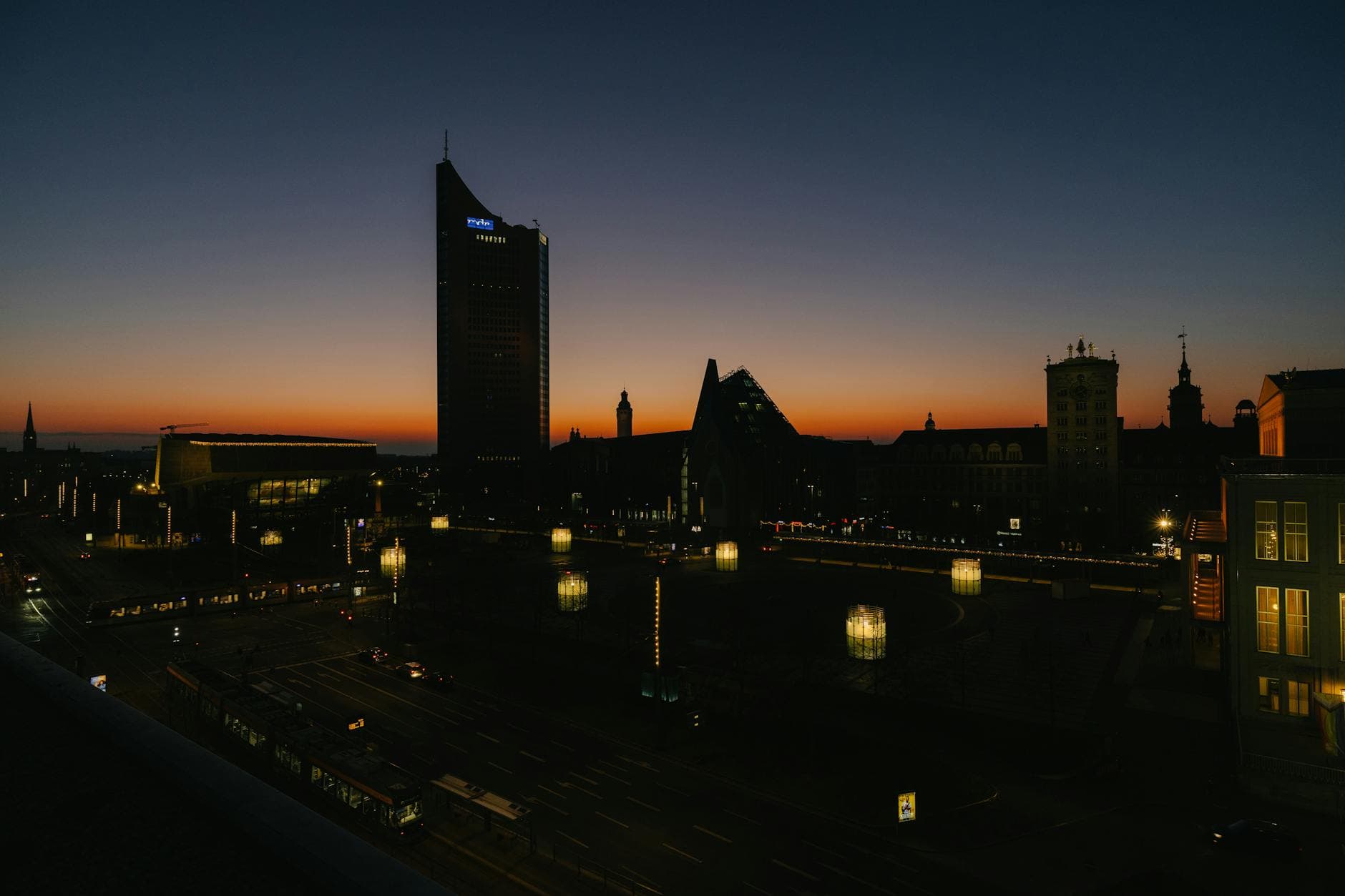 Dusk view of Leipzig's skyline with city lights and orange twilight sky.