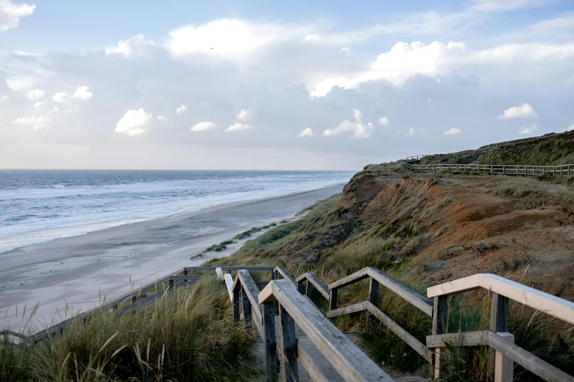 Explore the breathtaking view of Sylt with sandy beaches, cliffs, and a wooden pathway under a clear sky.